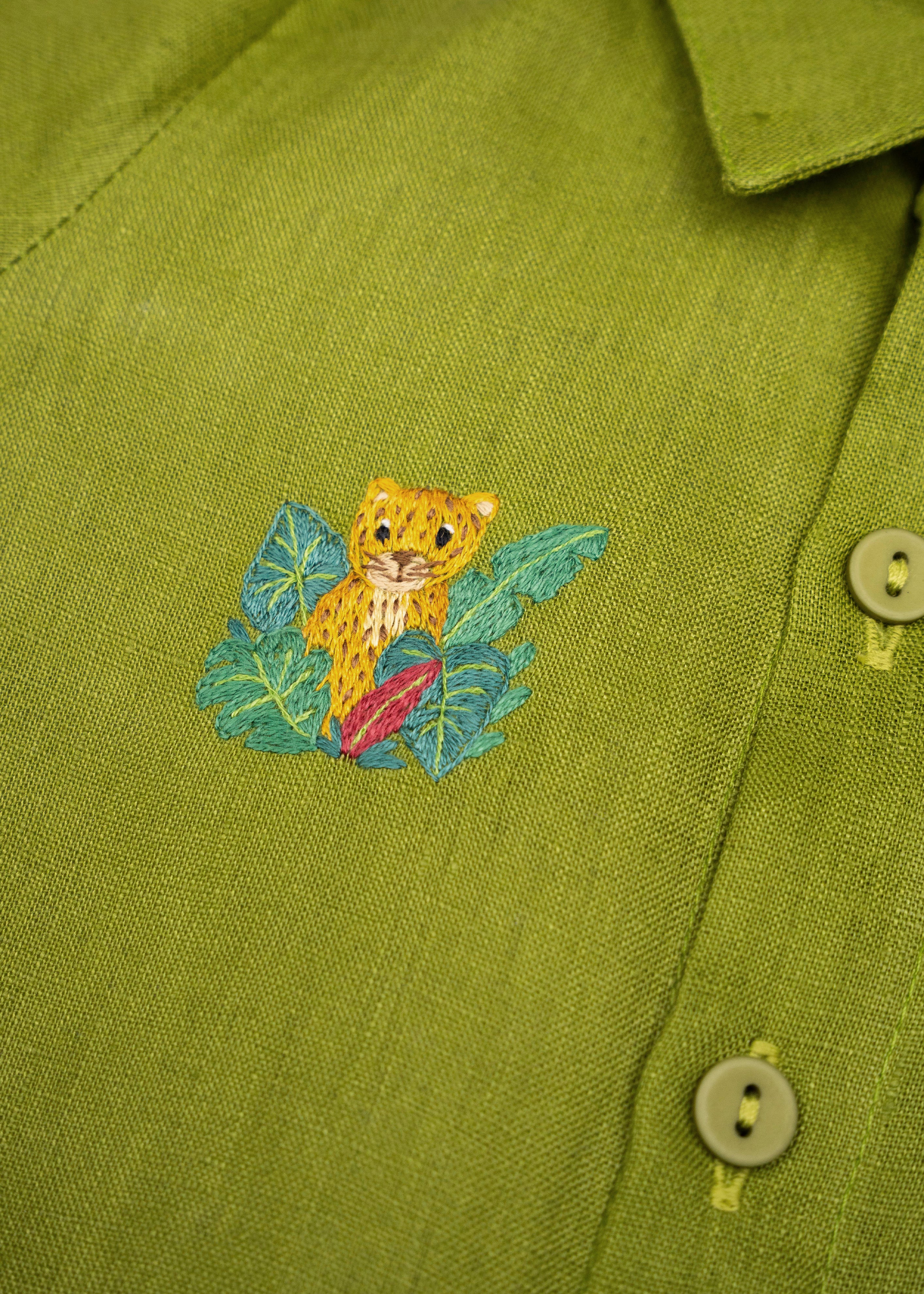 Detalhe do Macaquinho Tiê infantil em linho verde com onça entre folhagens bordada à mão.