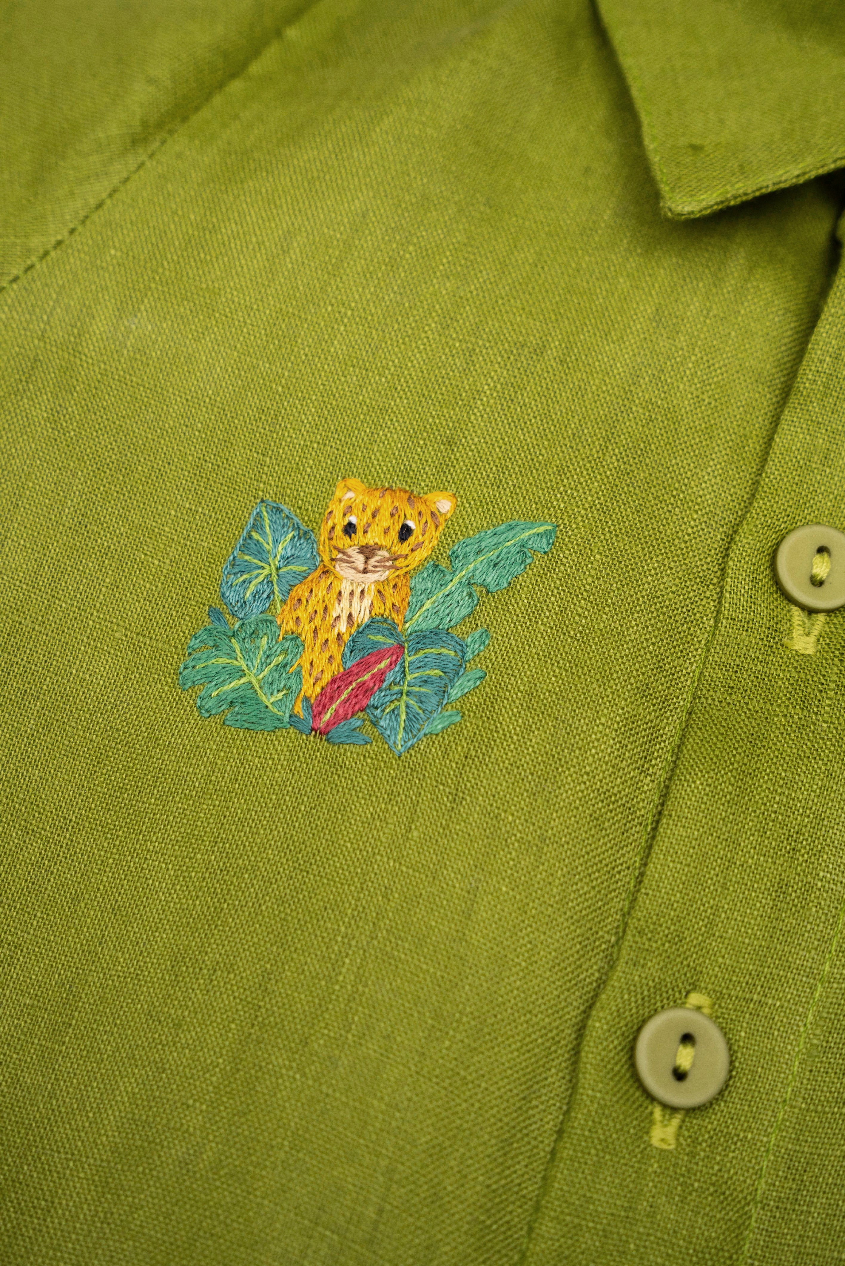 Detalhe do Macaquinho Tiê infantil em linho verde com onça entre folhagens bordada à mão.
