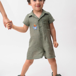 Menino vestindo Macaquinho Tiê infantil em 100% linho verde militar com bordado à mão dos Saltimbancos.
