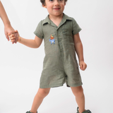 Menino vestindo Macaquinho Tiê infantil em 100% linho verde militar com bordado à mão dos Saltimbancos.