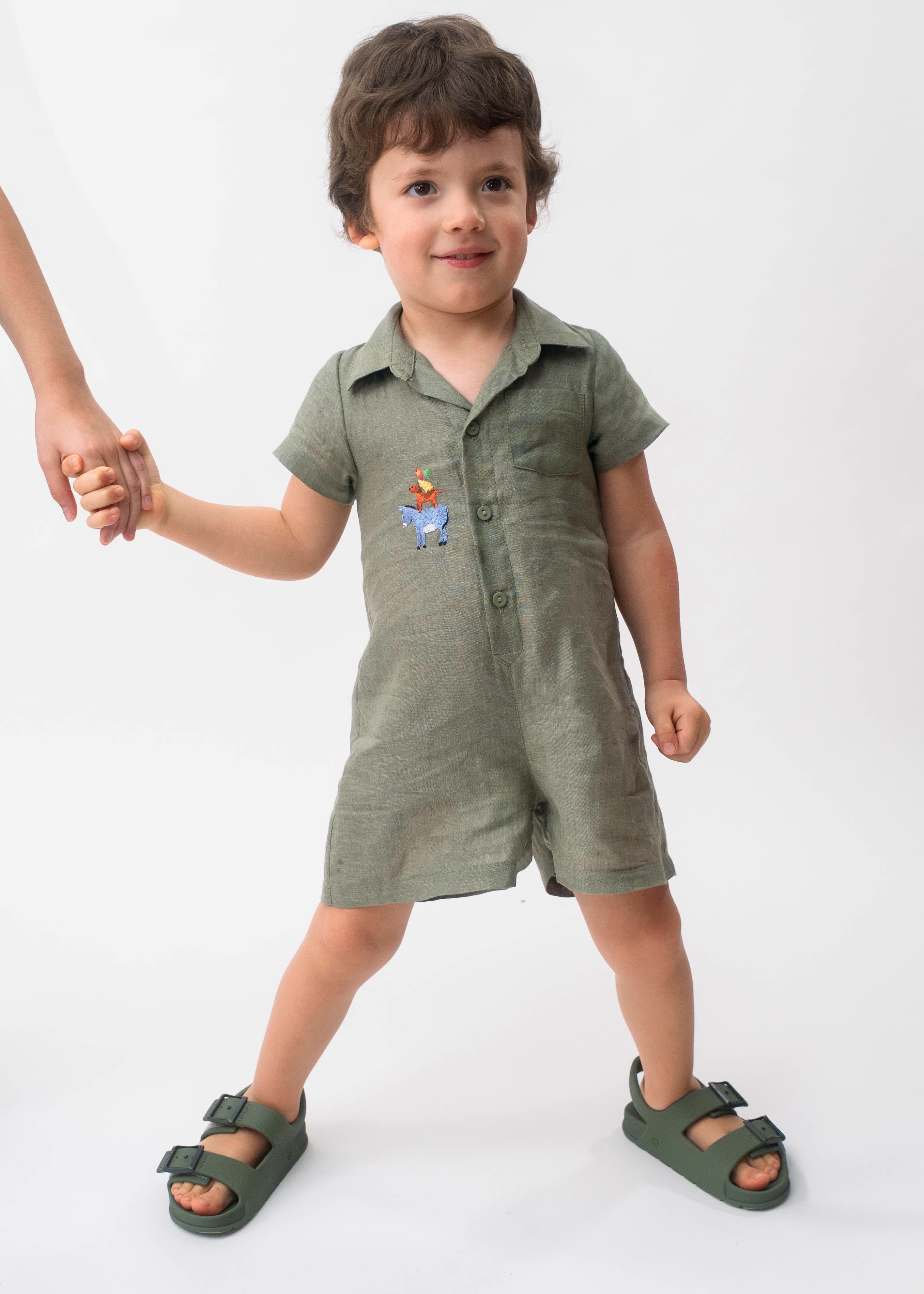 Menino vestindo Macaquinho Tiê infantil em 100% linho verde militar com bordado à mão dos Saltimbancos.