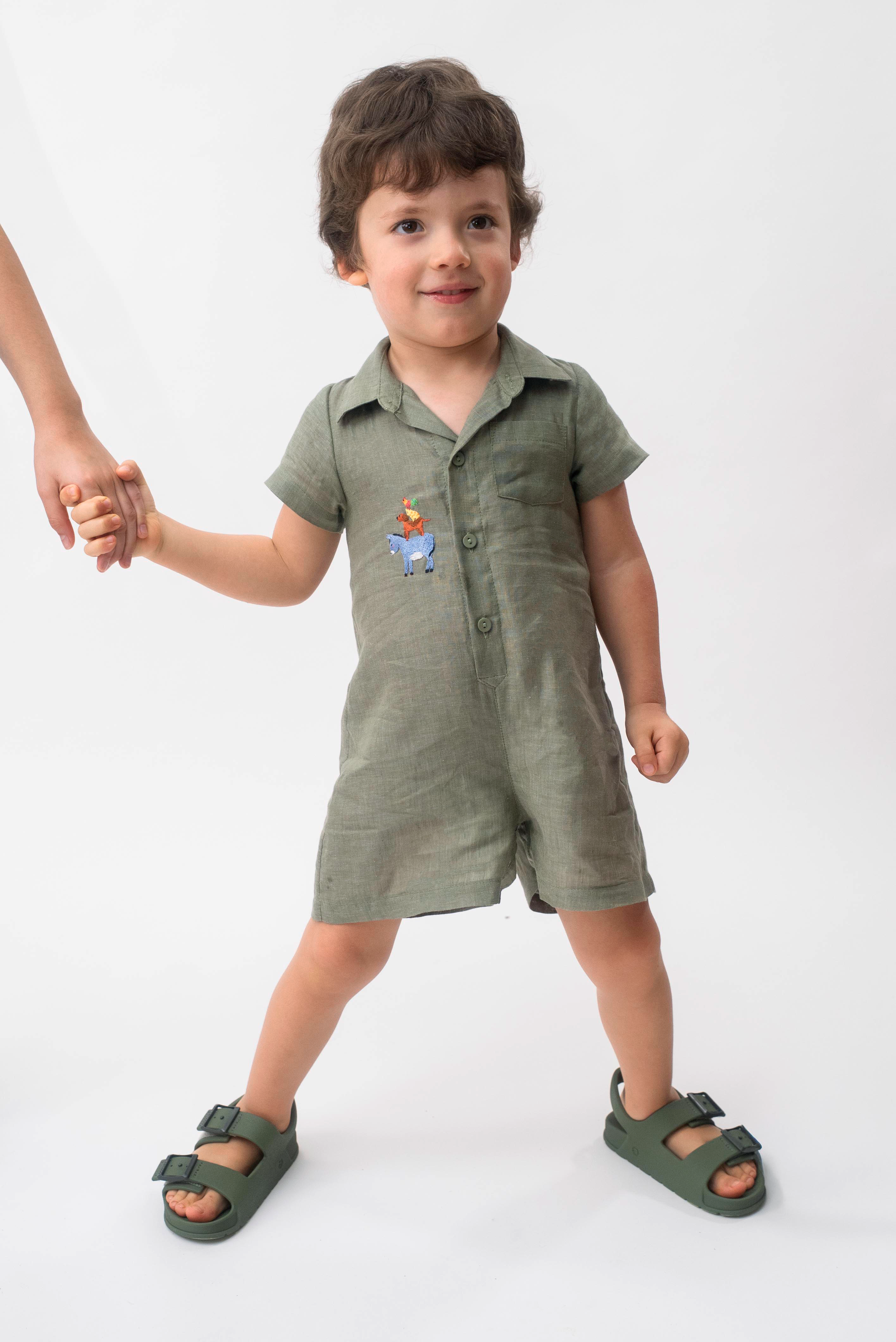 Menino vestindo Macaquinho Tiê infantil em 100% linho verde militar com bordado à mão dos Saltimbancos.