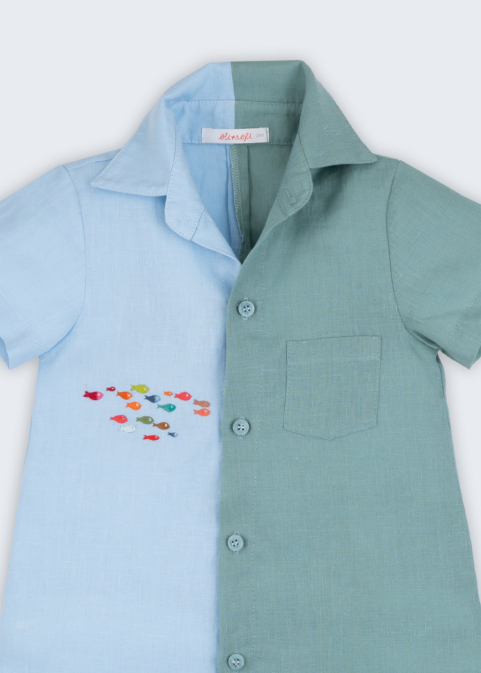 Macaquinho infantil em linho bicolor azul e verde com cardume de peixes bordado à mão, visto de frente em detalhe.