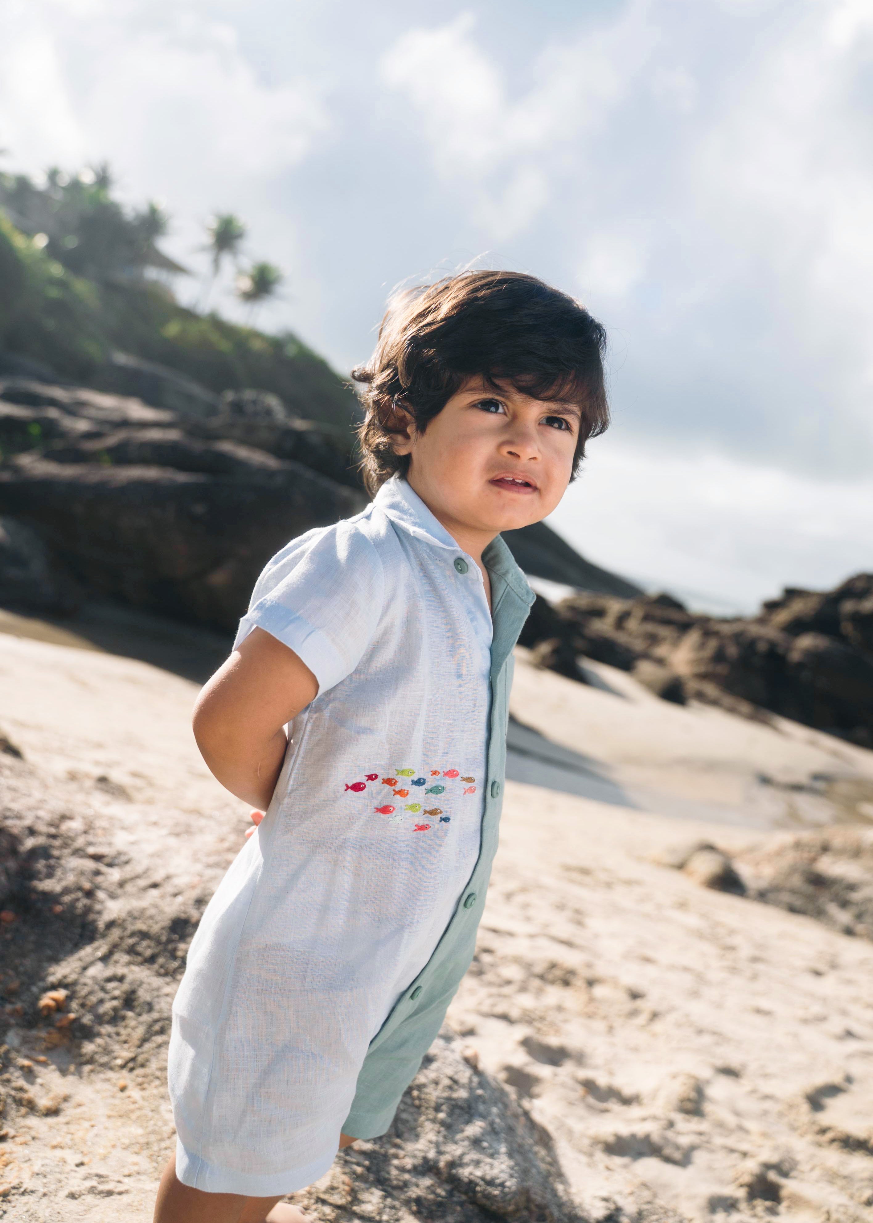 Menino com macaquinho de linho bicolor azul e verde com cardume de peixes bordado.