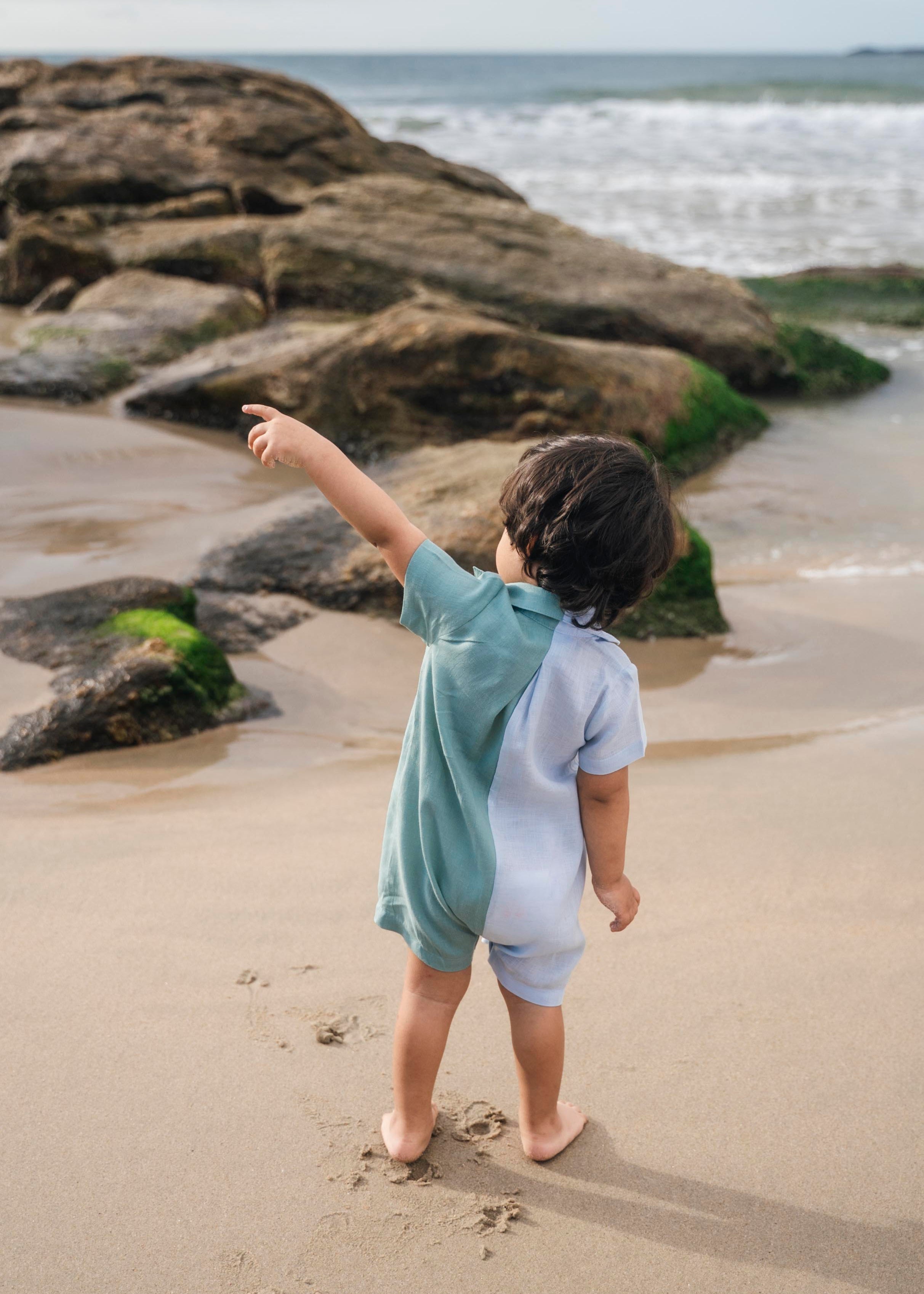 Menino de costas com macaquinho de linho bicolor azul e verde.