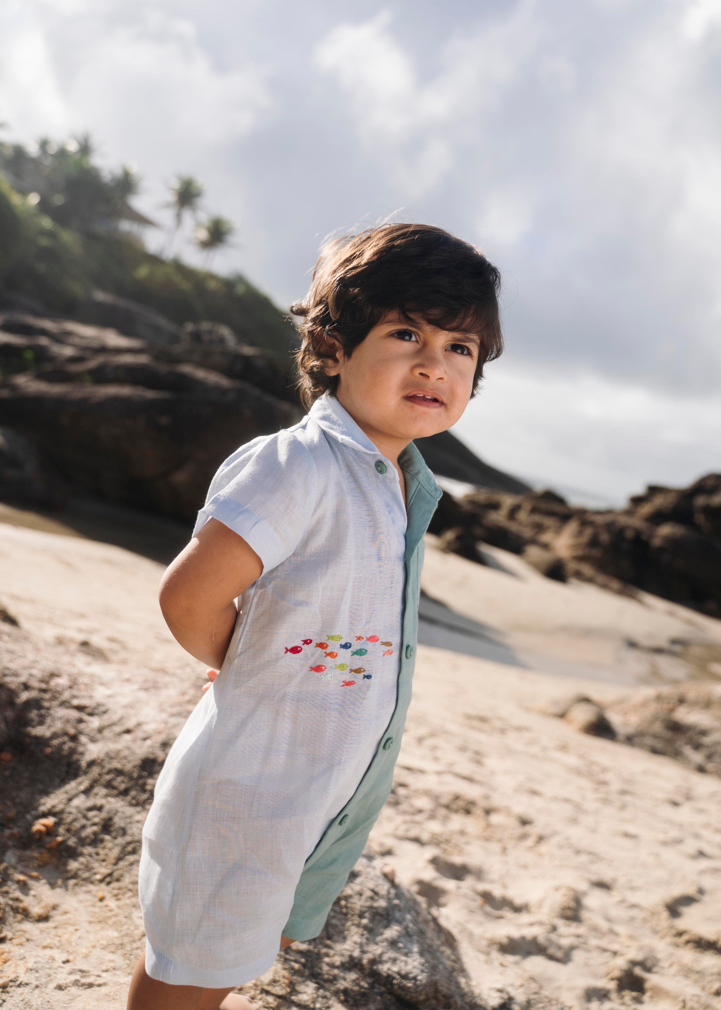 Menino com macaquinho de linho bicolor azul e verde com cardume de peixes bordado.