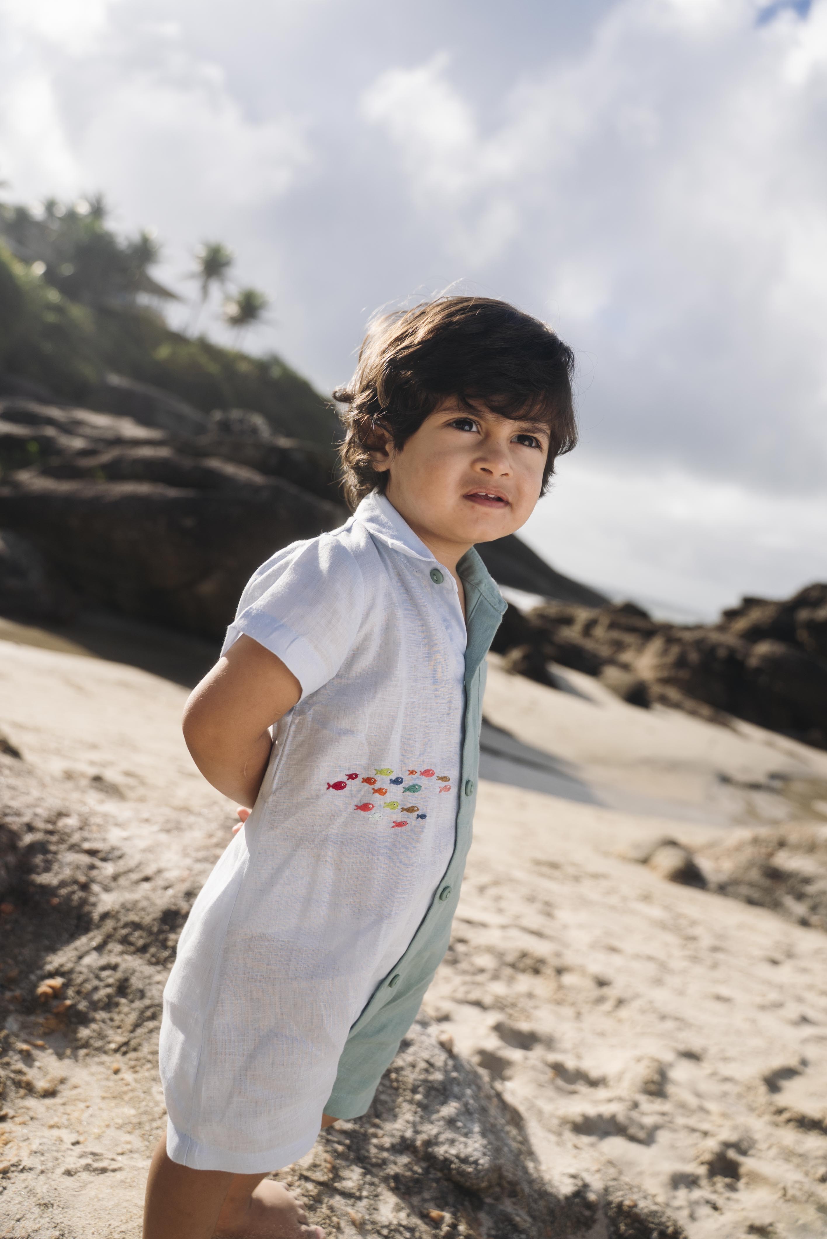 Menino com macaquinho de linho bicolor azul e verde com cardume de peixes bordado.