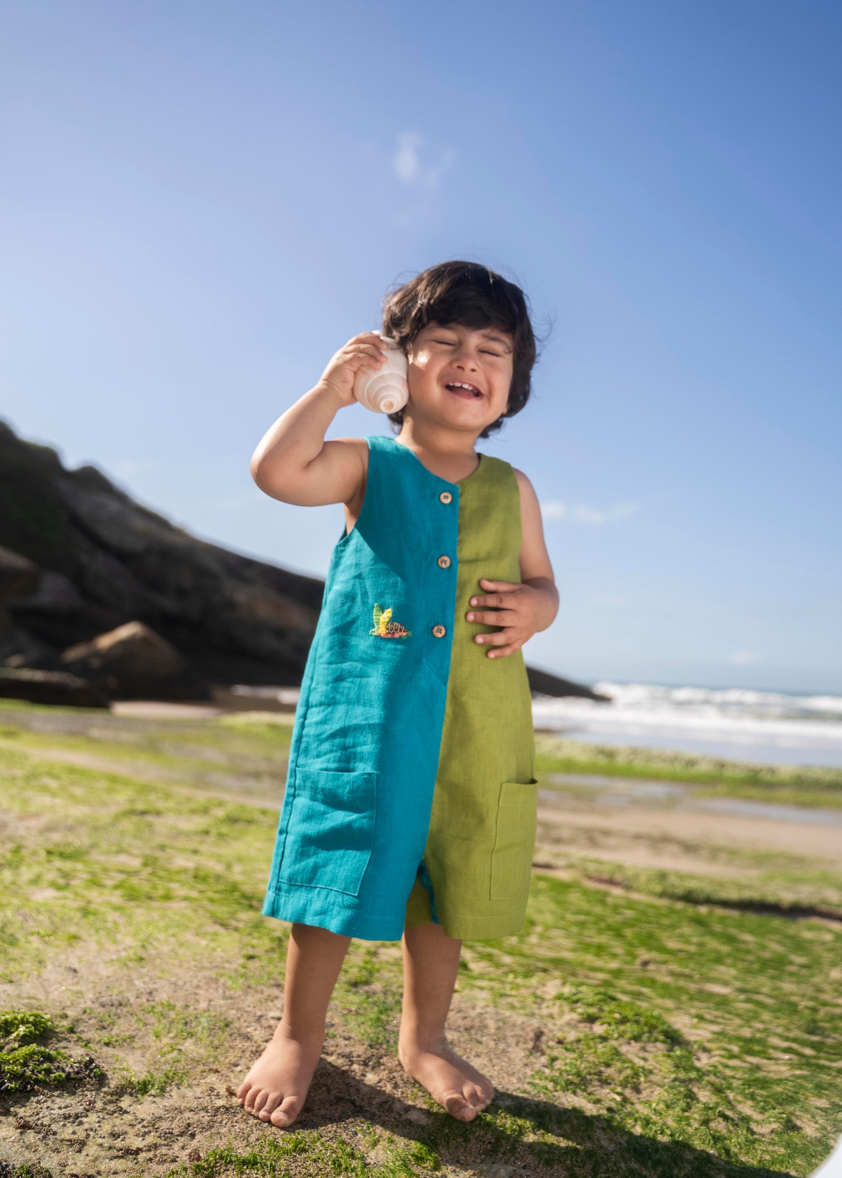 Menino usando macaquinho infantil em linho bicolor azul e verde com tartaruga bordada à mão.