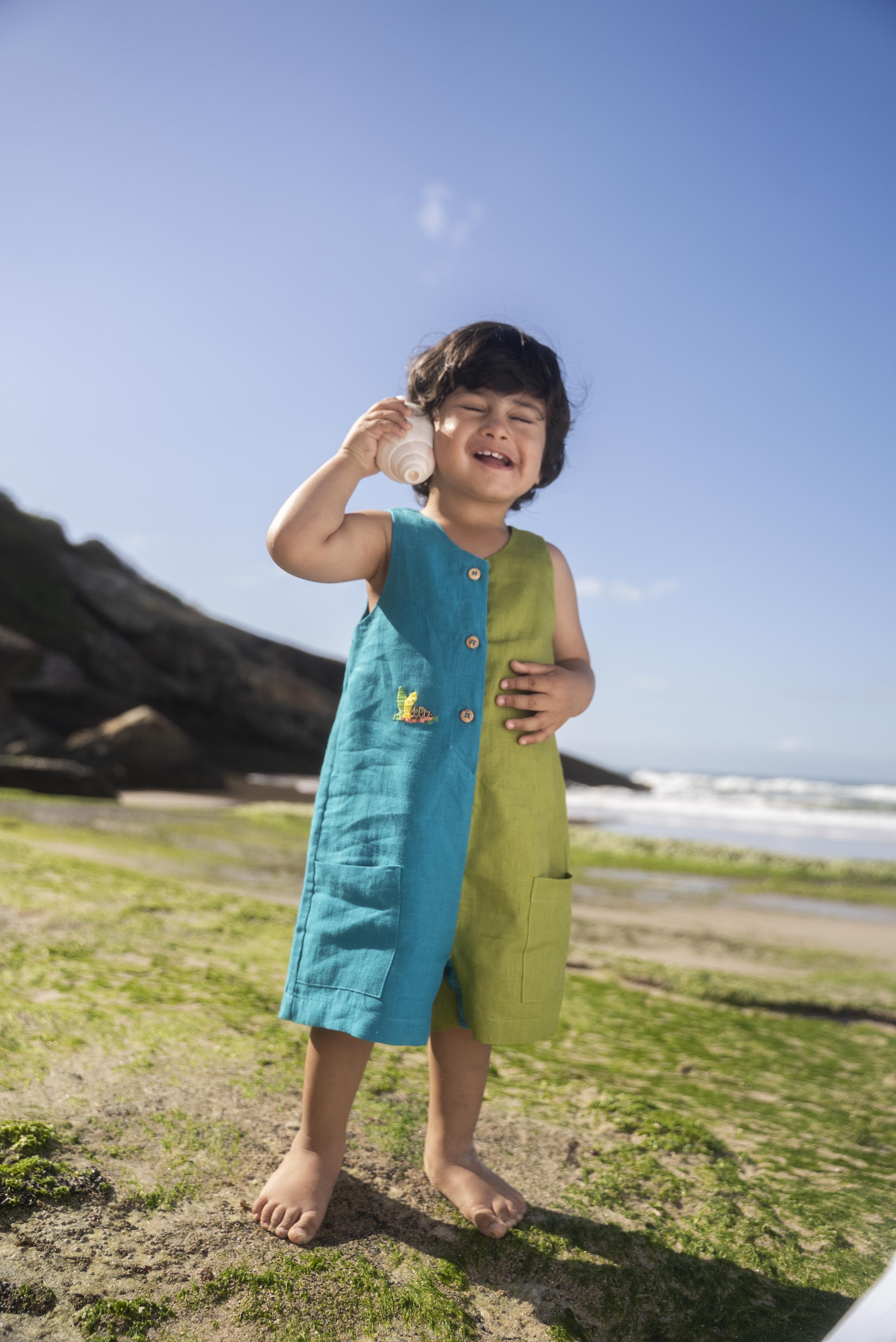 Menino usando macaquinho infantil em linho bicolor azul e verde com tartaruga bordada à mão.
