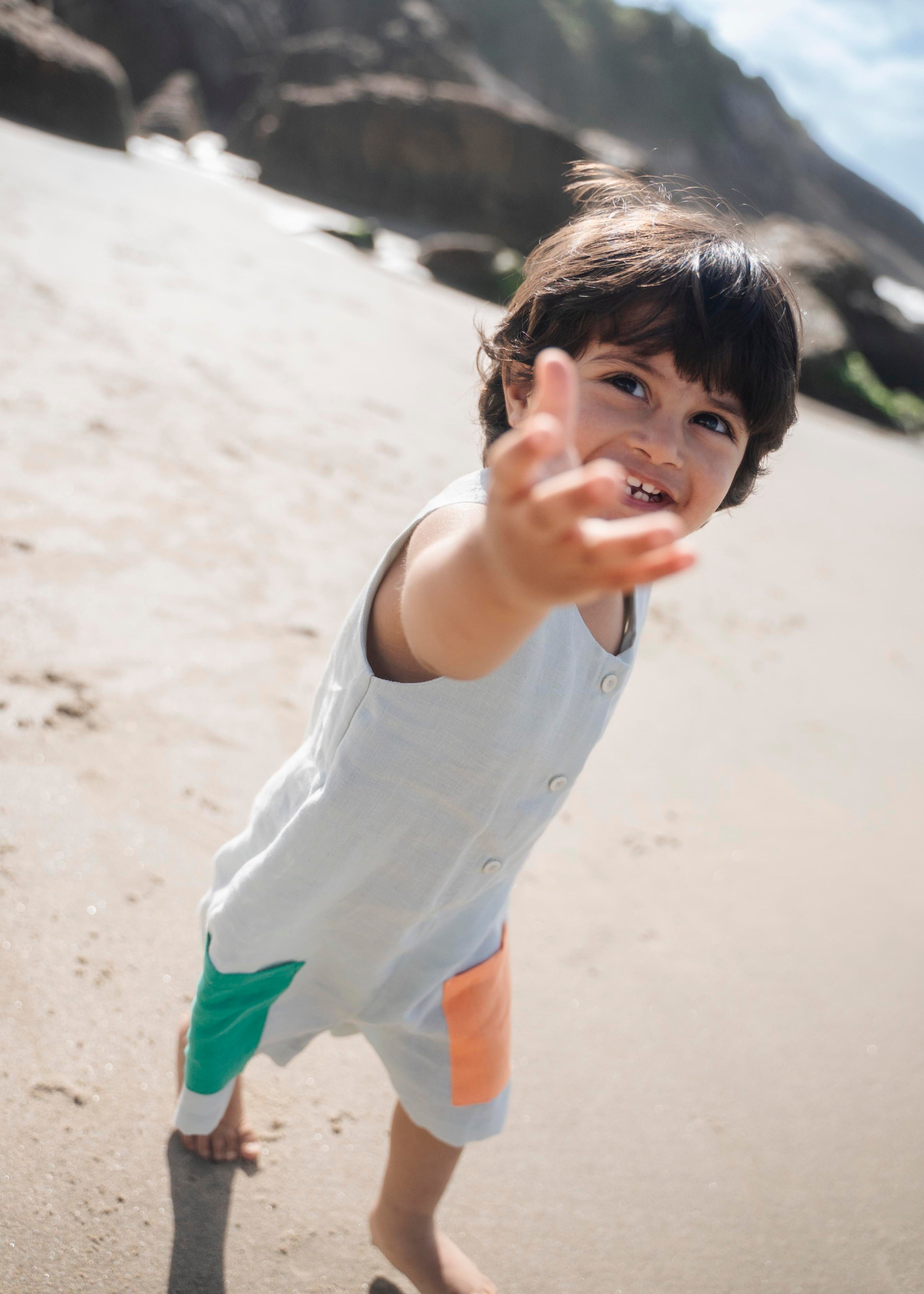 Menino com macaquinho infantil em linho gelo com bolsos coloridos verde e laranja.