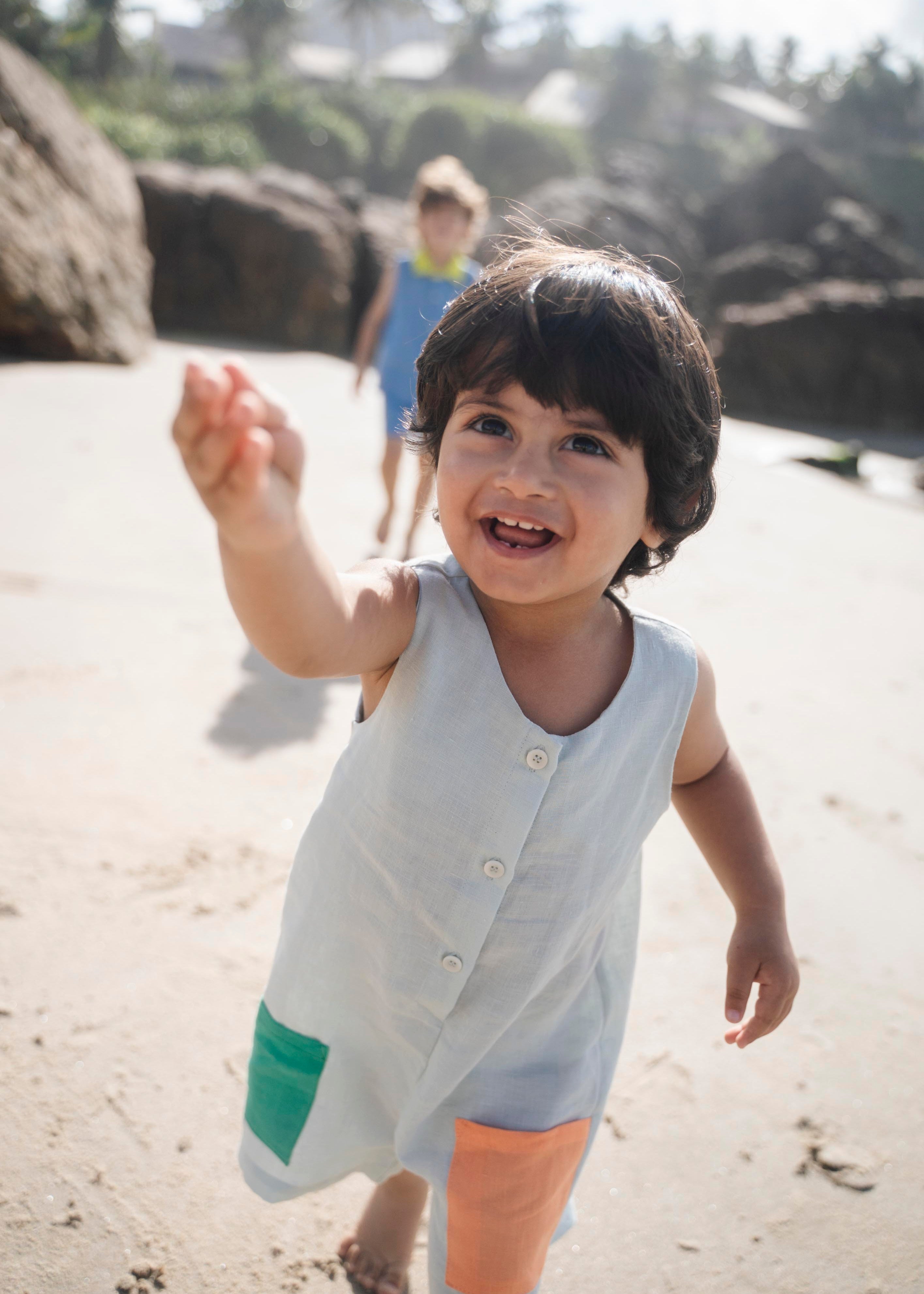 Menino com macaquinho infantil em linho puro na cor gelo com bolsos coloridos.