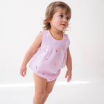 Bebê menina vestindo macaquinho infantil de linho rosa estilo romper, com flores coloridas bordadas à mão.