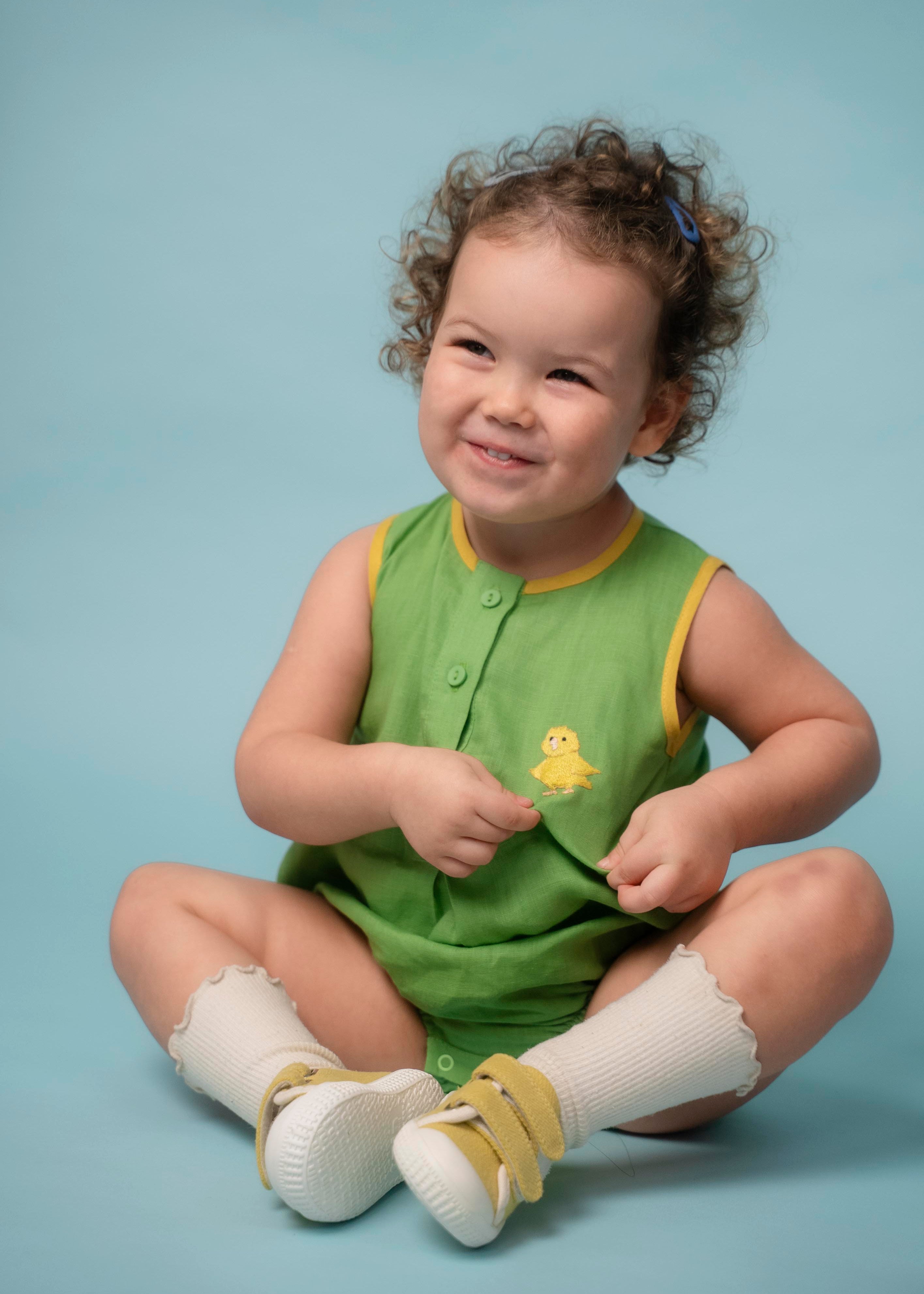 Bebê usando macaquinho verde em linho puro com bordado de canarinho e acabamento amarelo