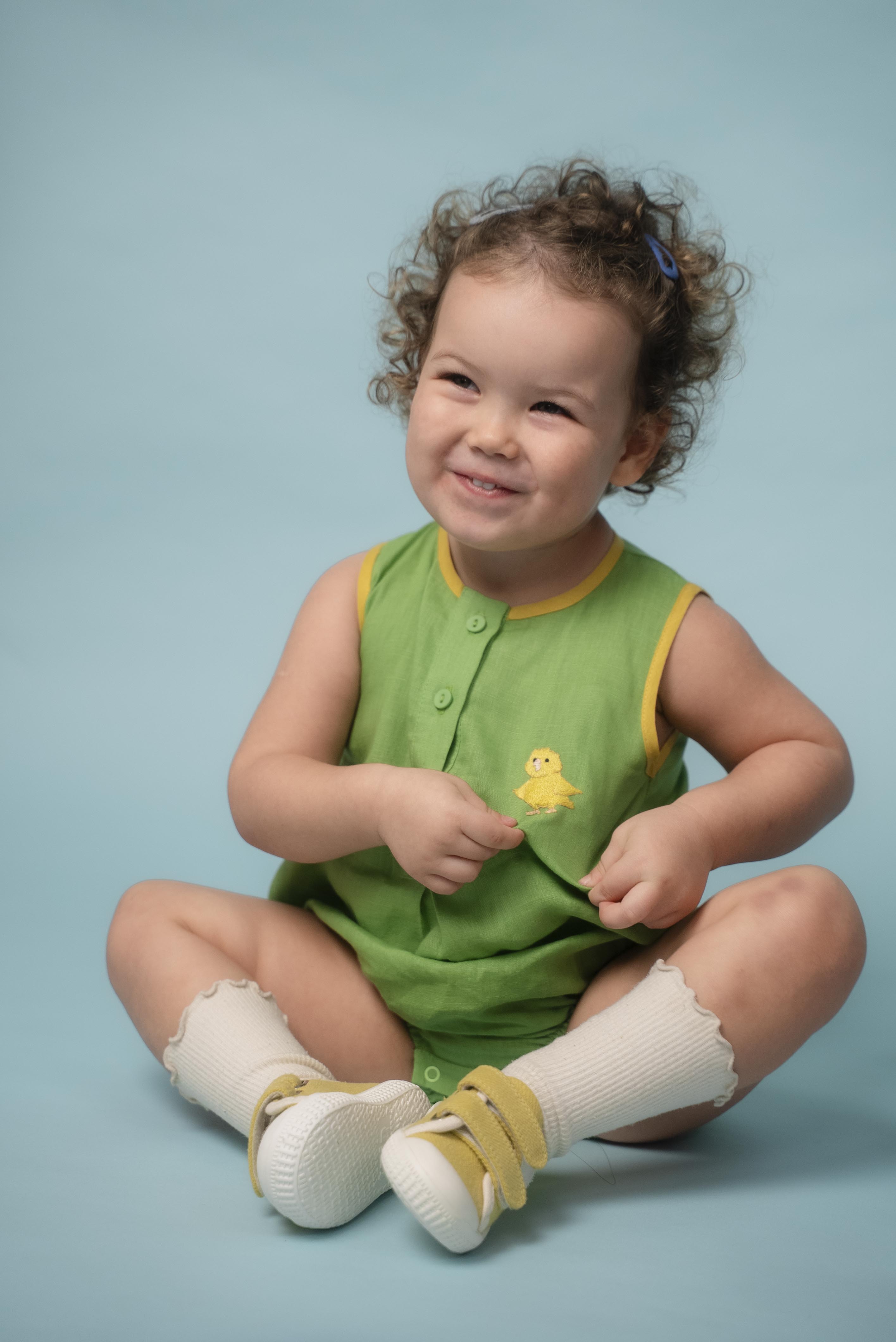 Bebê usando macaquinho verde em linho puro com bordado de canarinho e acabamento amarelo