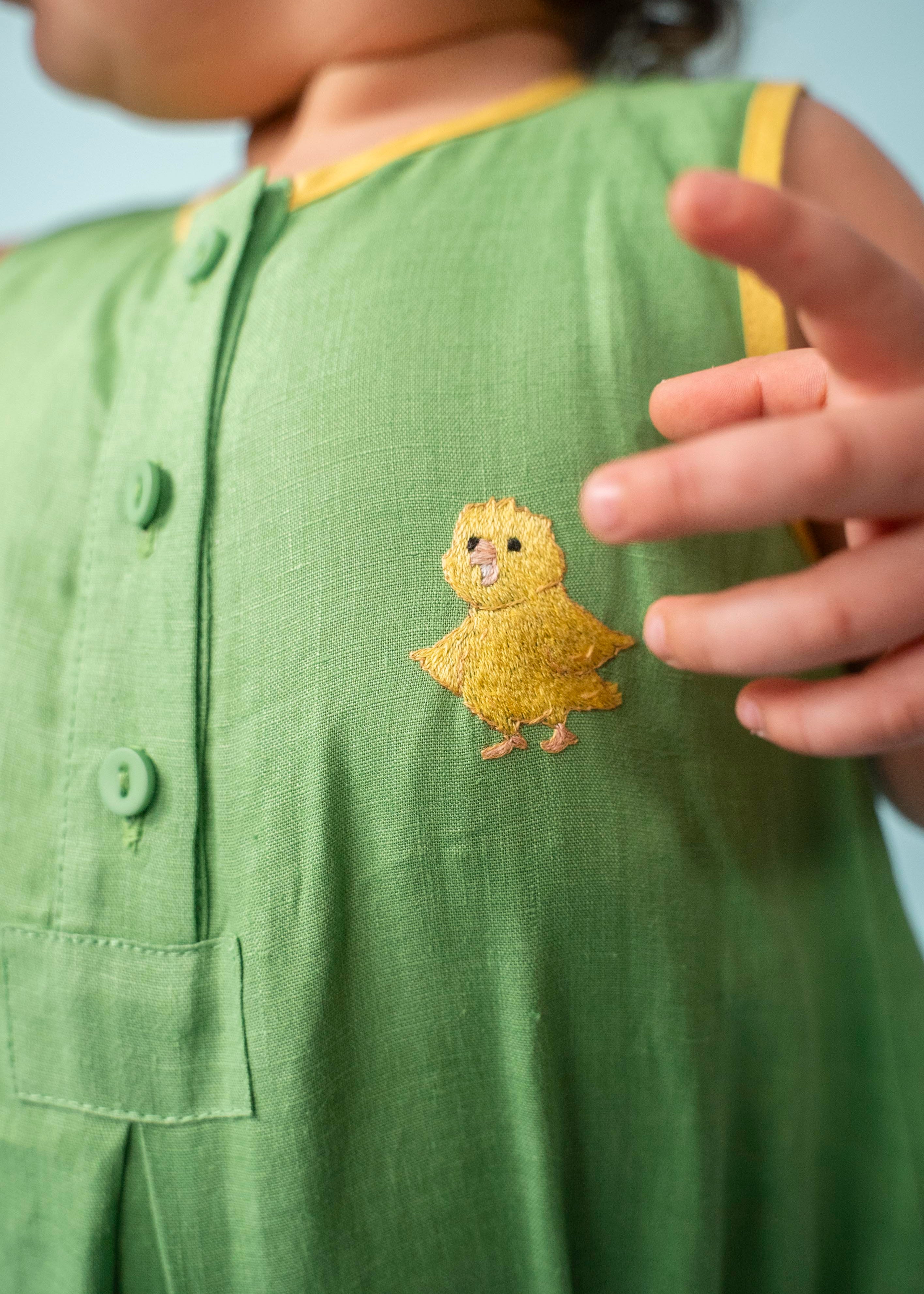 Detalhe do canarinho bordado à mão no peito do macaquinho de bebê verde bandeira de linho puro