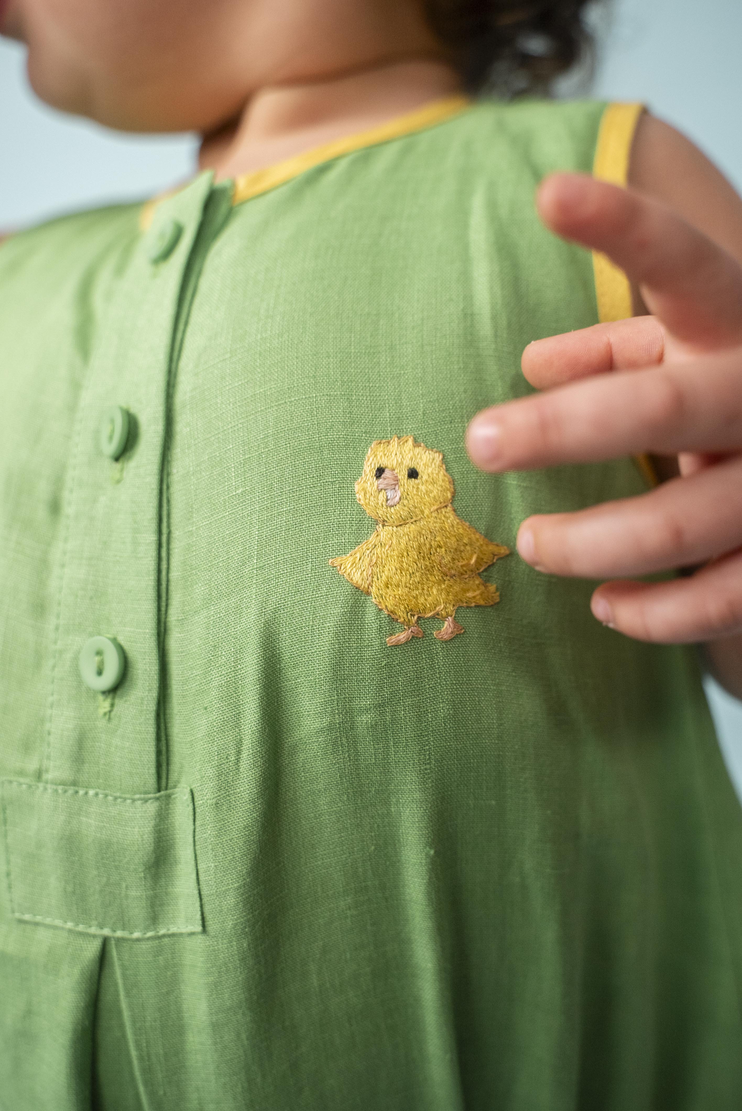 Detalhe do canarinho bordado à mão no peito do macaquinho de bebê verde bandeira de linho puro