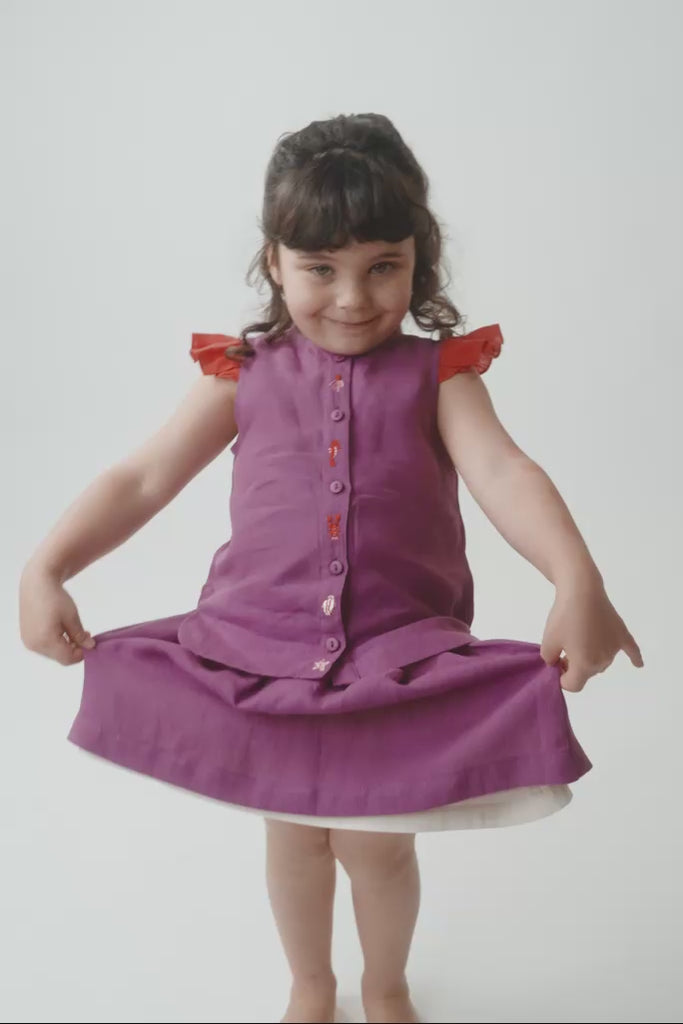 Menina usando camisa clara roxa coordenada com saia em mesmo tom, mostrando o caimento, o tecido de linho e os detalhes bordados na carcela.