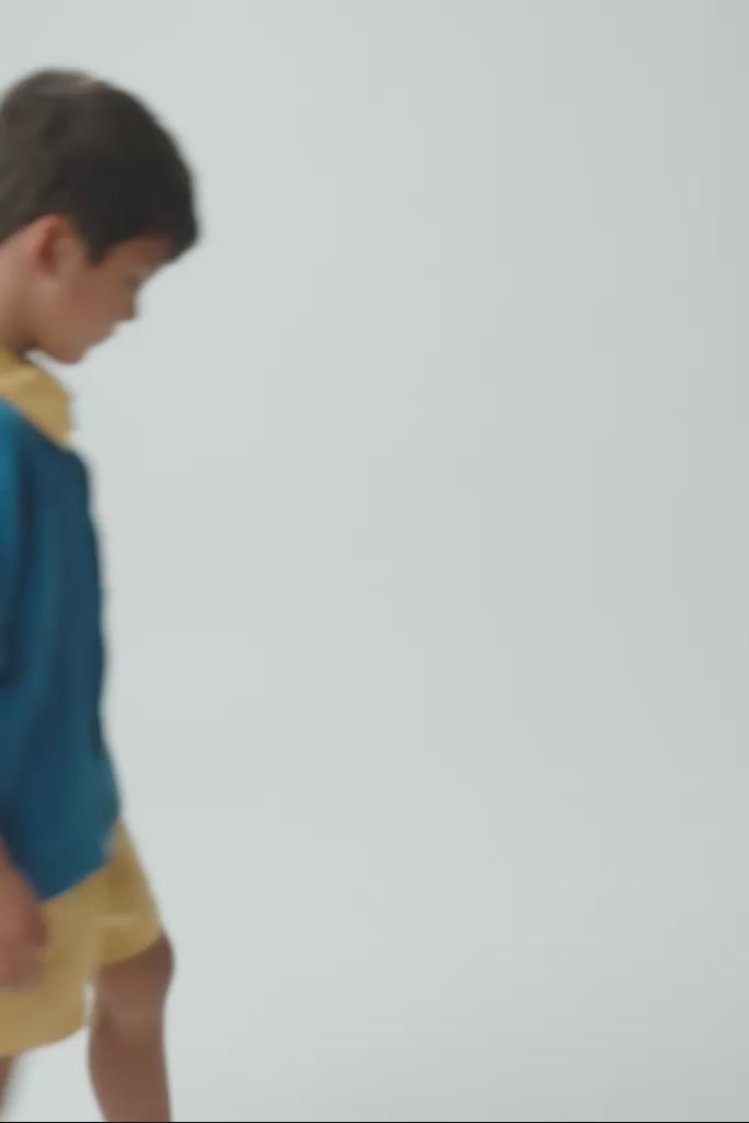 Criança em movimento usando camisa Tom com bordado de onça, mostrando o caimento da peça e os detalhes feitos à mão.