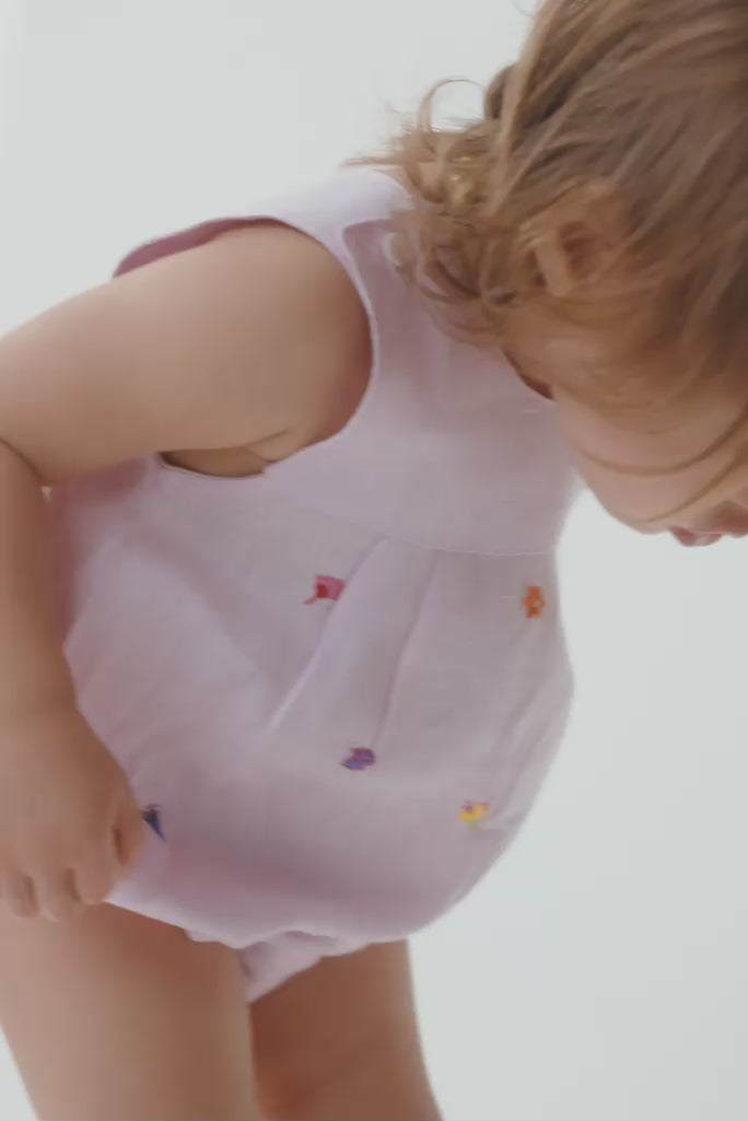 Menina bebê usando macaquinho estilo romper, mostrando o caimento, o tecido de linho e os detalhes das flores bordadas à mão.