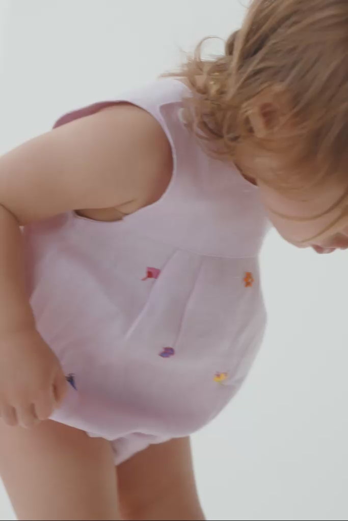 Menina bebê usando macaquinho estilo romper, mostrando o caimento, o tecido de linho e os detalhes das flores bordadas à mão.