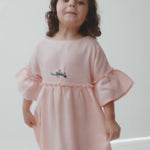 Menina em movimento usando vestido Pietra rosa, mostrando o caimento da peça e os detalhes feitos à mão.