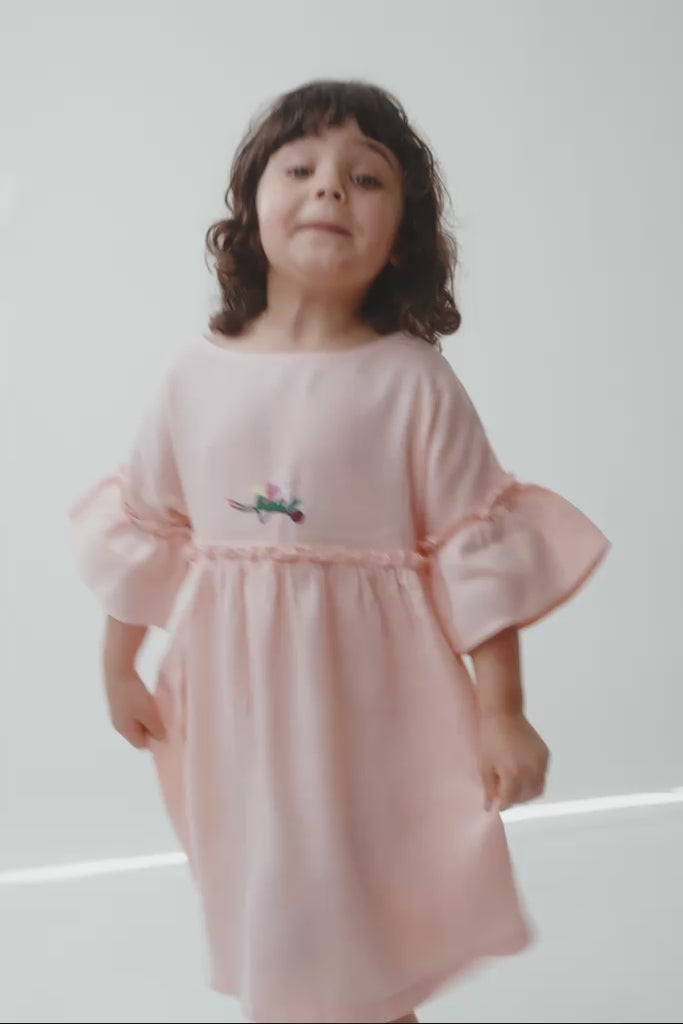 Menina em movimento usando vestido Pietra rosa, mostrando o caimento da peça e os detalhes feitos à mão.