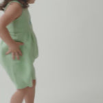 Menina em movimento usando macaquinho infância, mostrando o caimento da peça e os detalhes feitos à mão.