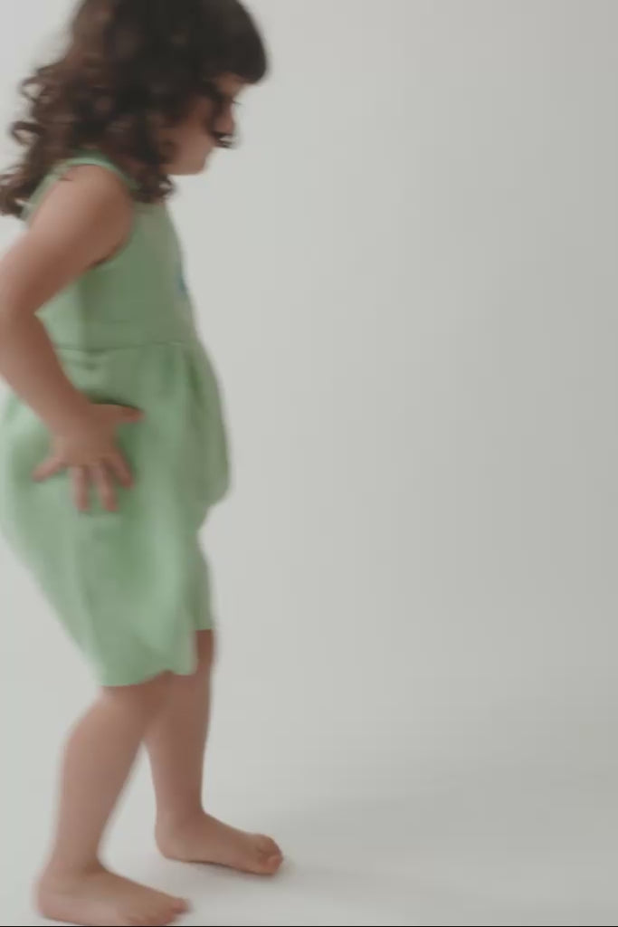 Menina em movimento usando macaquinho infância, mostrando o caimento da peça e os detalhes feitos à mão.