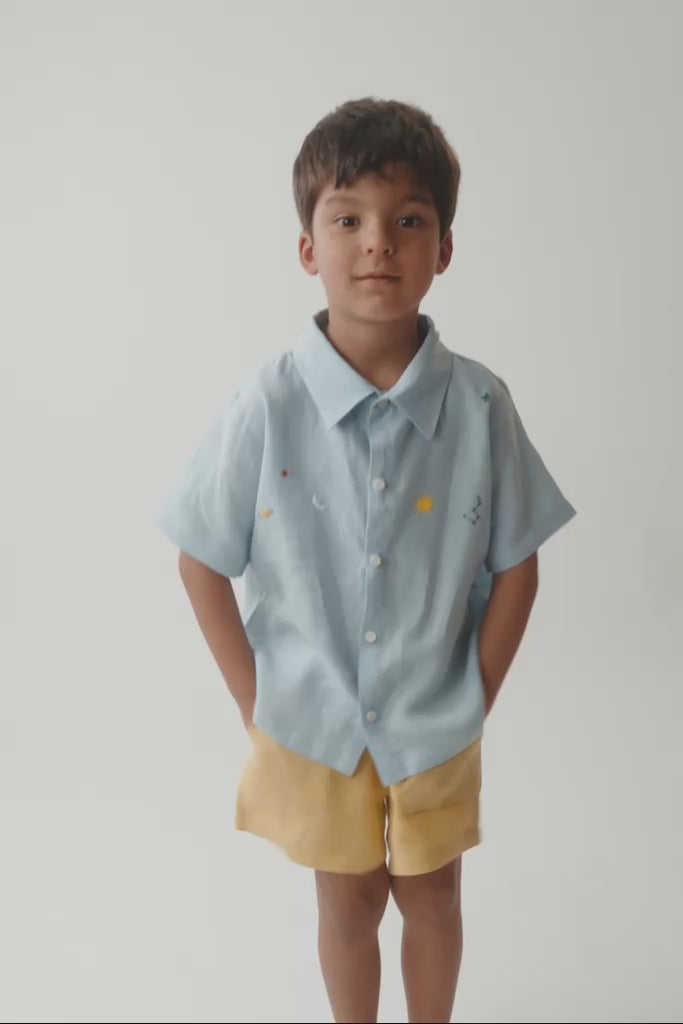 Menino vestindo camisa em linho azul bebê, com close nos detalhes do bordado e acabamento.