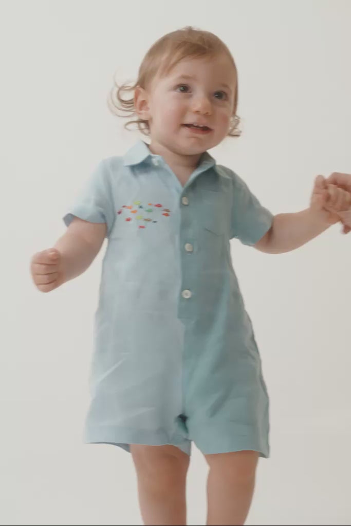 Criança em movimento usando macaquinho tiê bicolor azul, mostrando o caimento da peça e os detalhes feitos à mão.