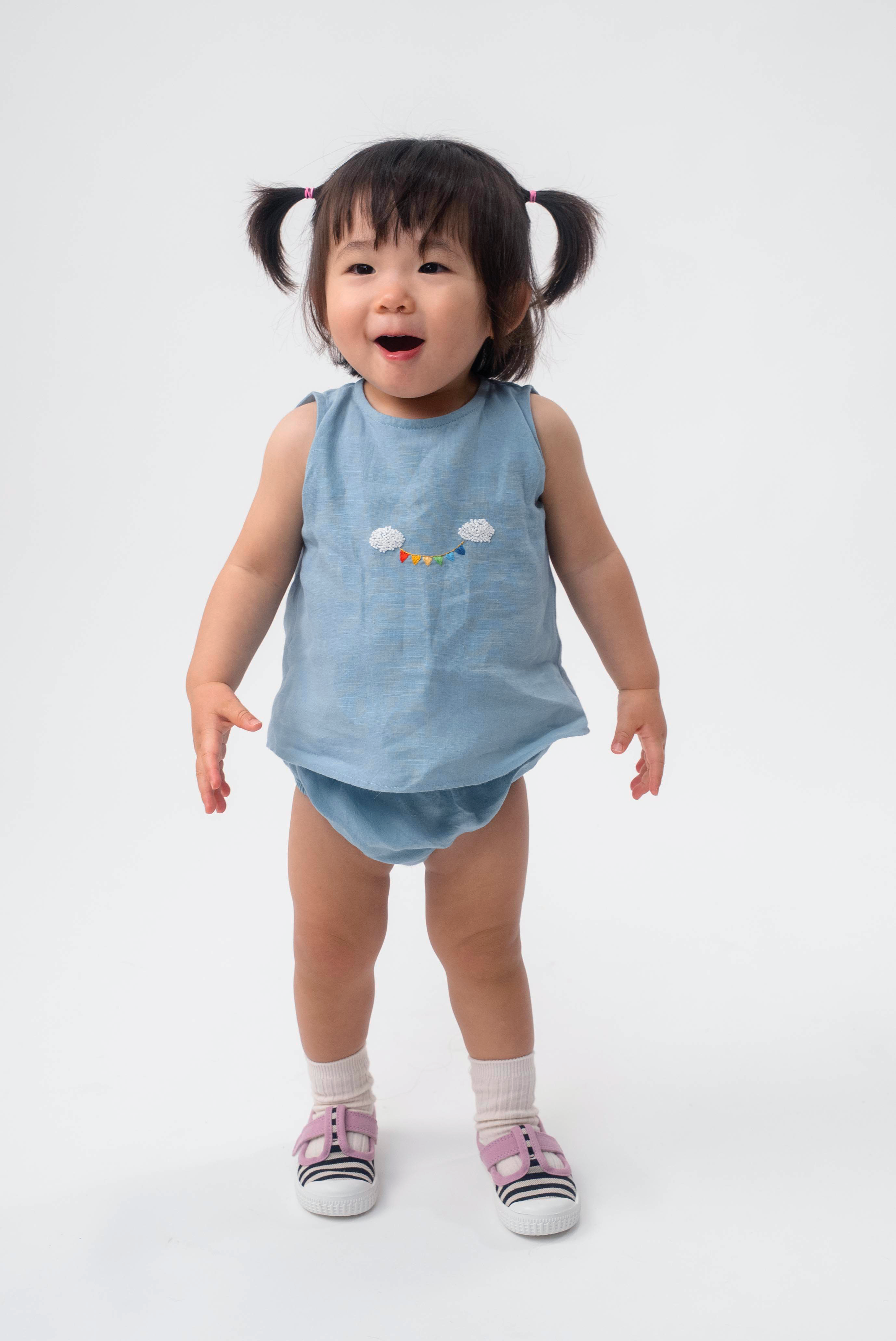 Bebê vestindo Conjunto Duda em linho azul celeste, com regata bordada à mão e tapa-fralda.