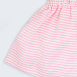 Detalhe da saia infantil em linho listrado rosa e branco, mostrando tecido leve com listras finas e cintura elástica.