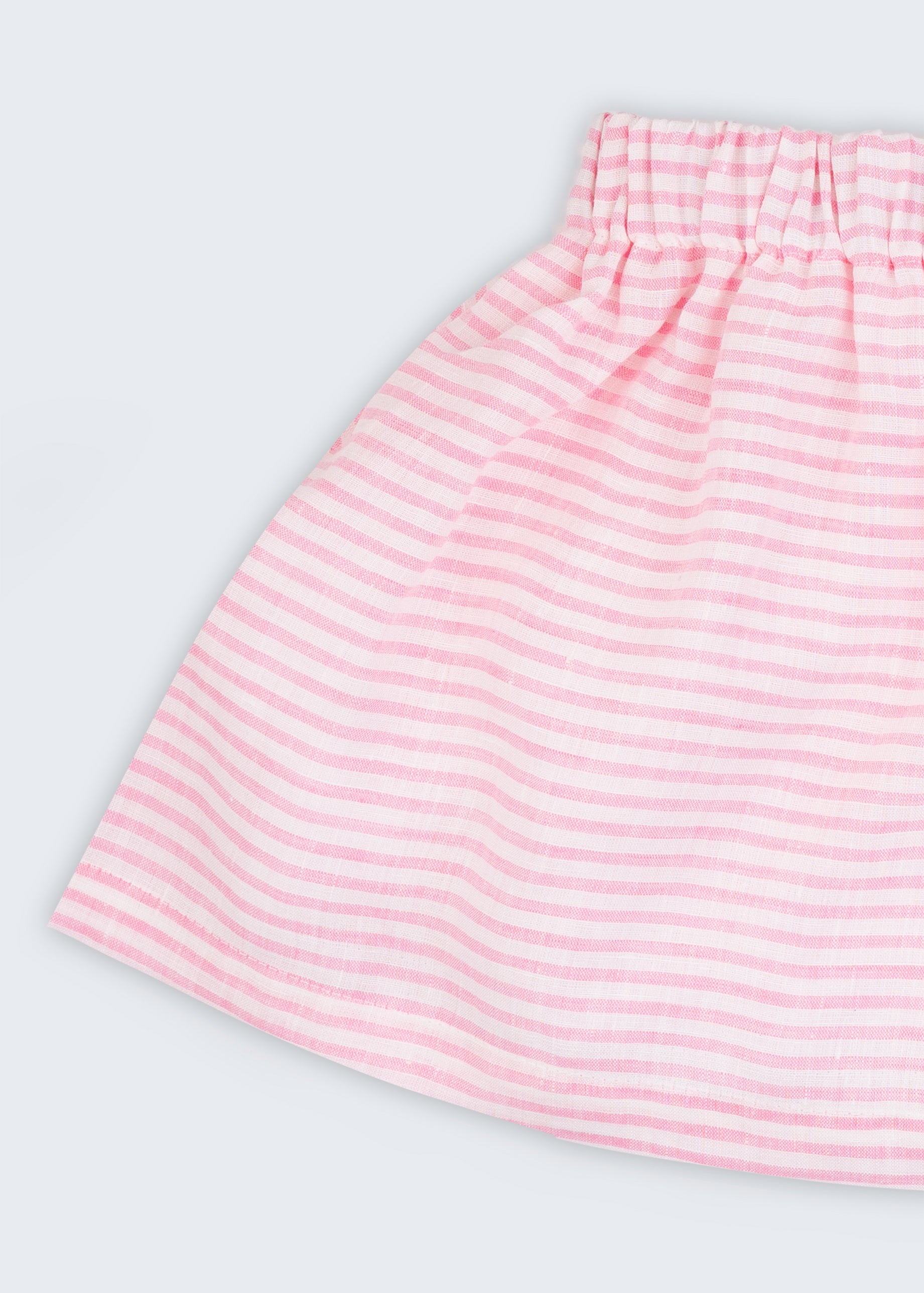 Detalhe da saia infantil em linho listrado rosa e branco, mostrando tecido leve com listras finas e cintura elástica.