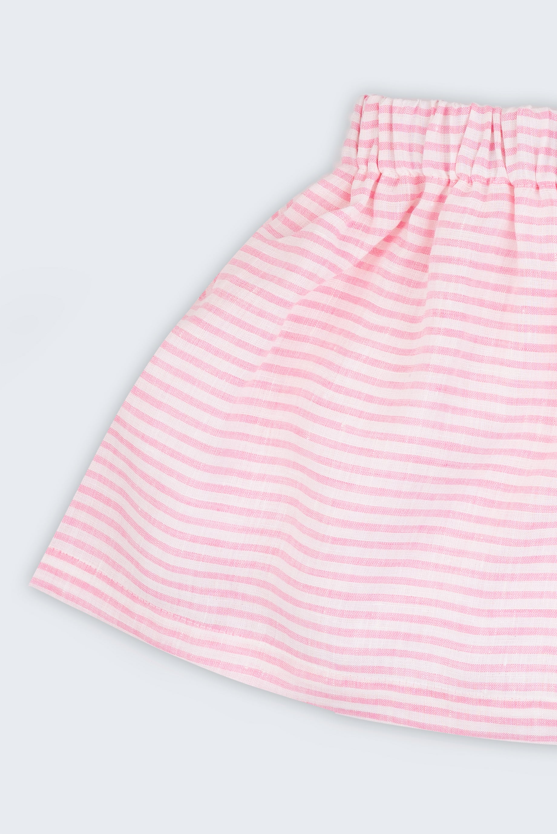 Detalhe da saia infantil em linho listrado rosa e branco, mostrando tecido leve com listras finas e cintura elástica.