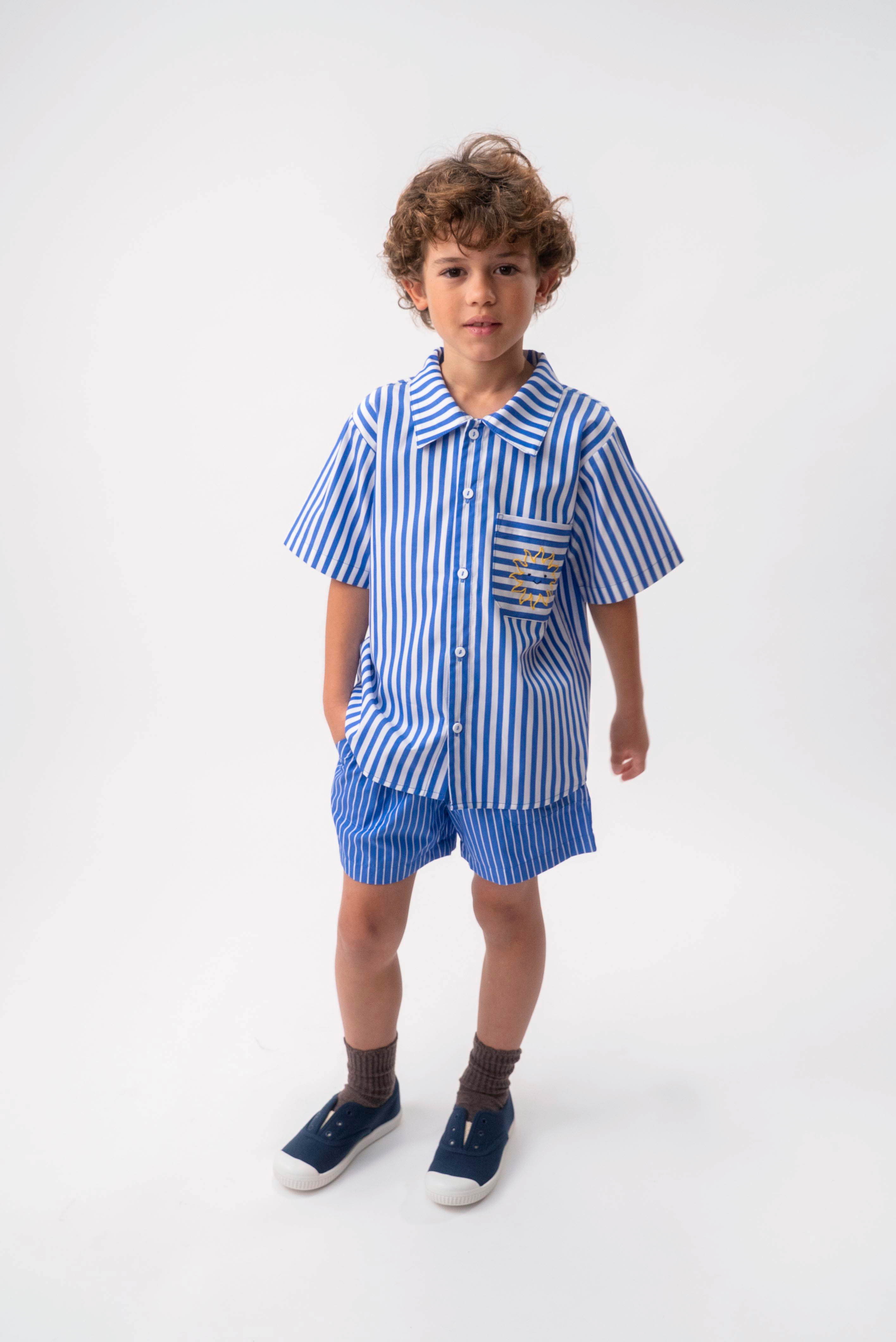 Menino vestindo Shorts Chico infantil em algodão azul com listras brancas, combinado com camisa listrada.