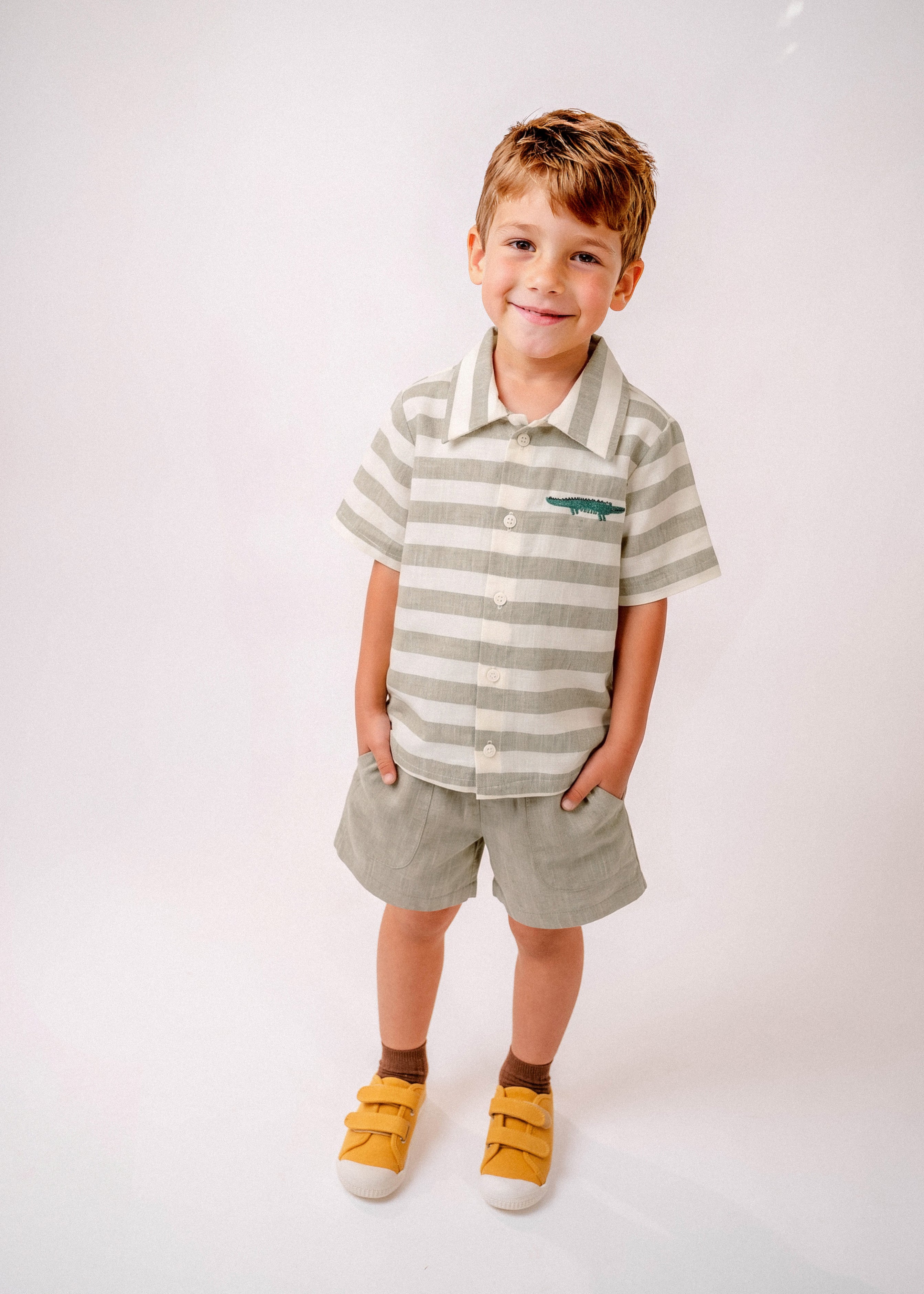 Menino vestindo shorts infantil verde oliva com camisa listrada em mesmo tom com bordado de jacaré