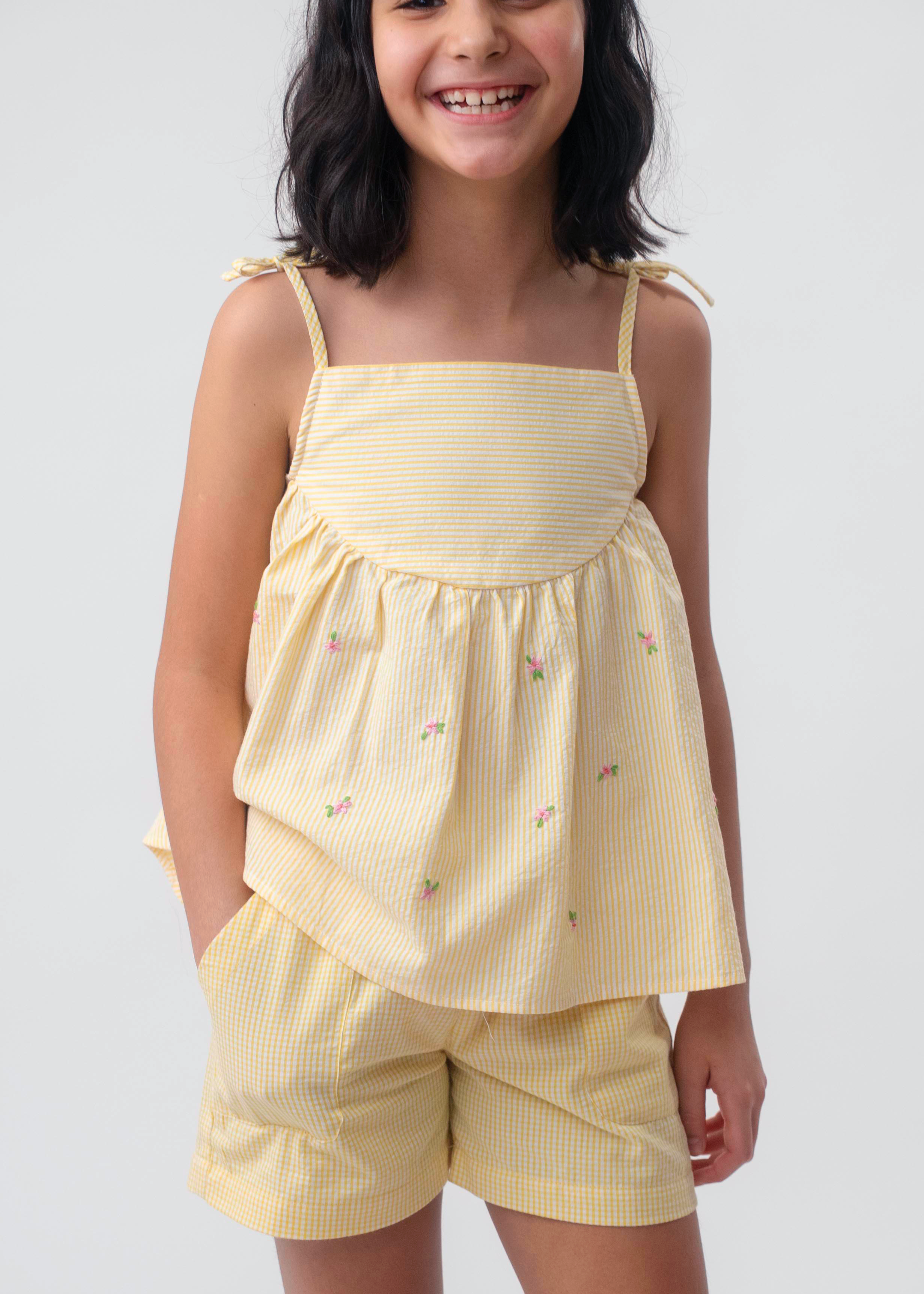 Menina vestindo Shorts Chico infantil xadrez amarelo em algodão, combinado com bata no mesmo tecido.