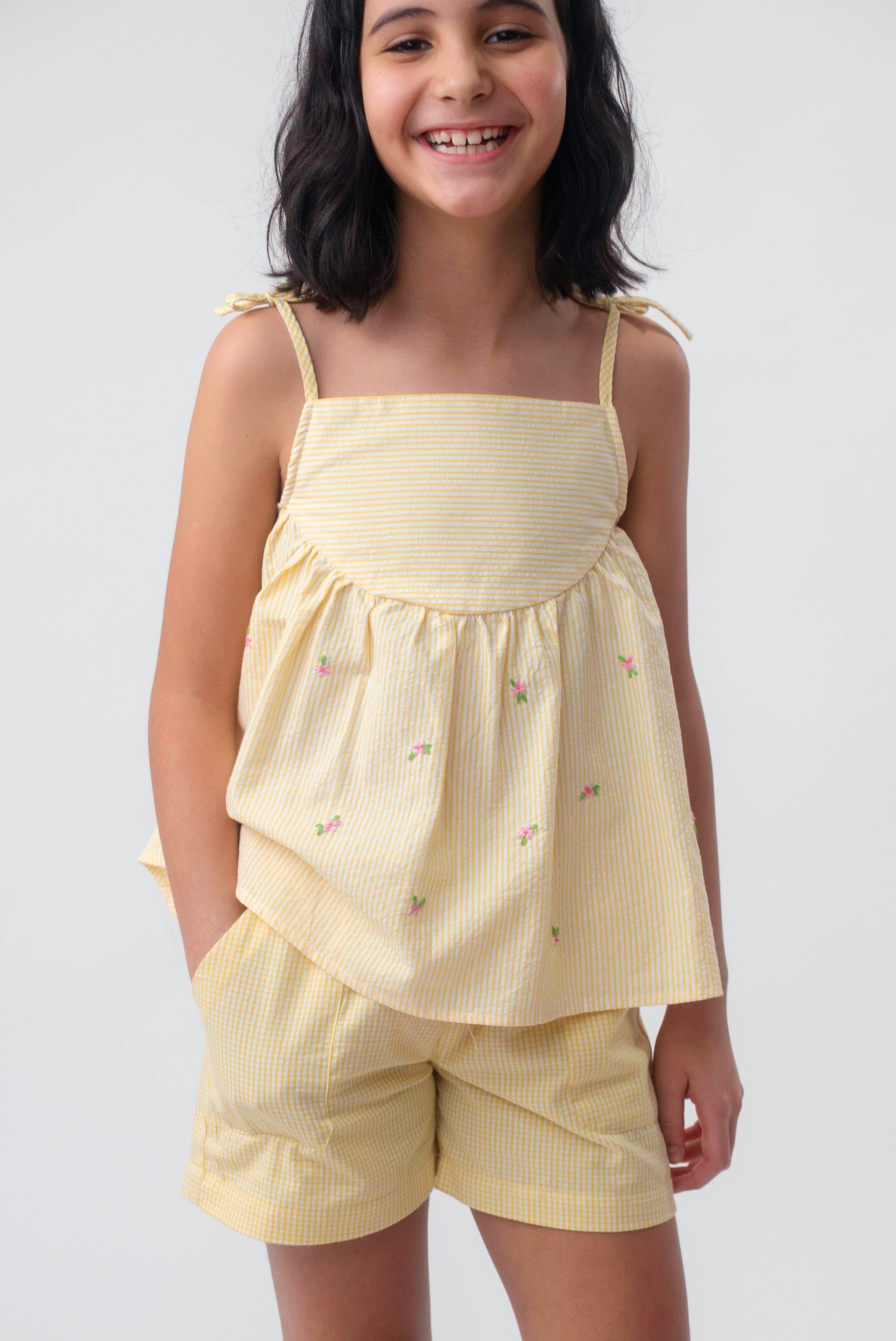 Menina vestindo Shorts Chico infantil xadrez amarelo em algodão, combinado com bata no mesmo tecido.