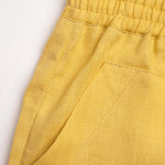 Detalhe do shorts infantil em linho amarelo com bolso frontal e cintura de elástico