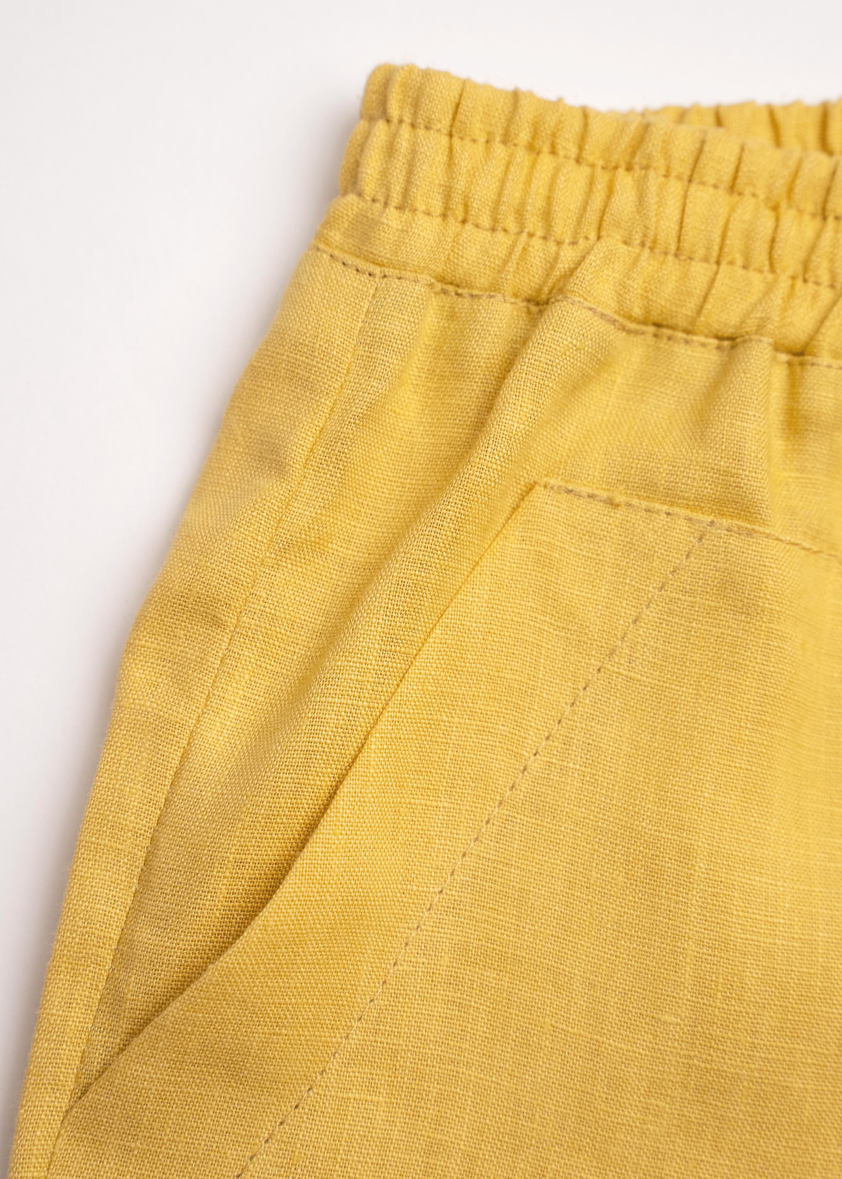 Detalhe do shorts infantil em linho amarelo com bolso frontal e cintura de elástico