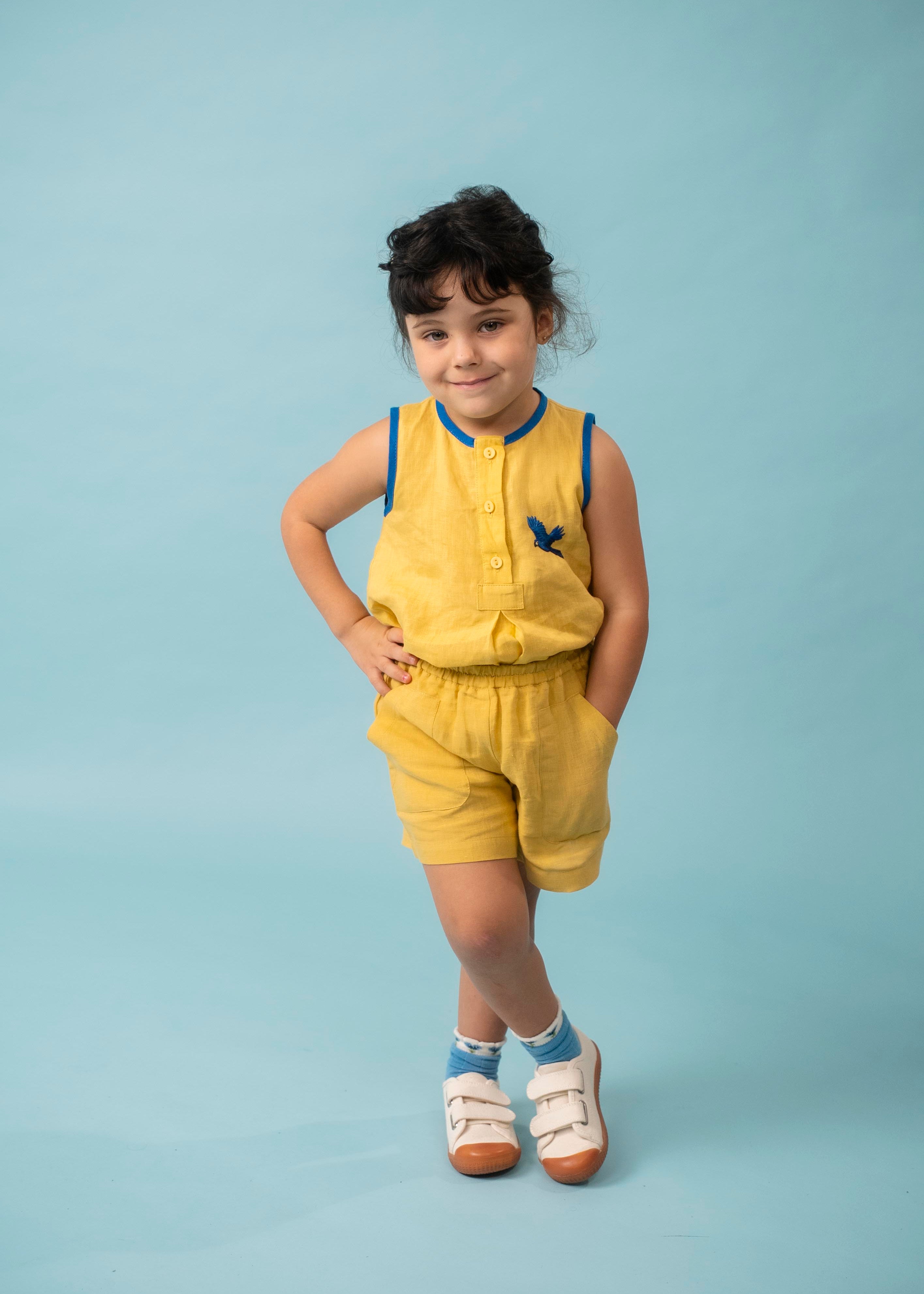 Menina usando shorts infantil amarelo em linho puro com blusa bordada de arara azul