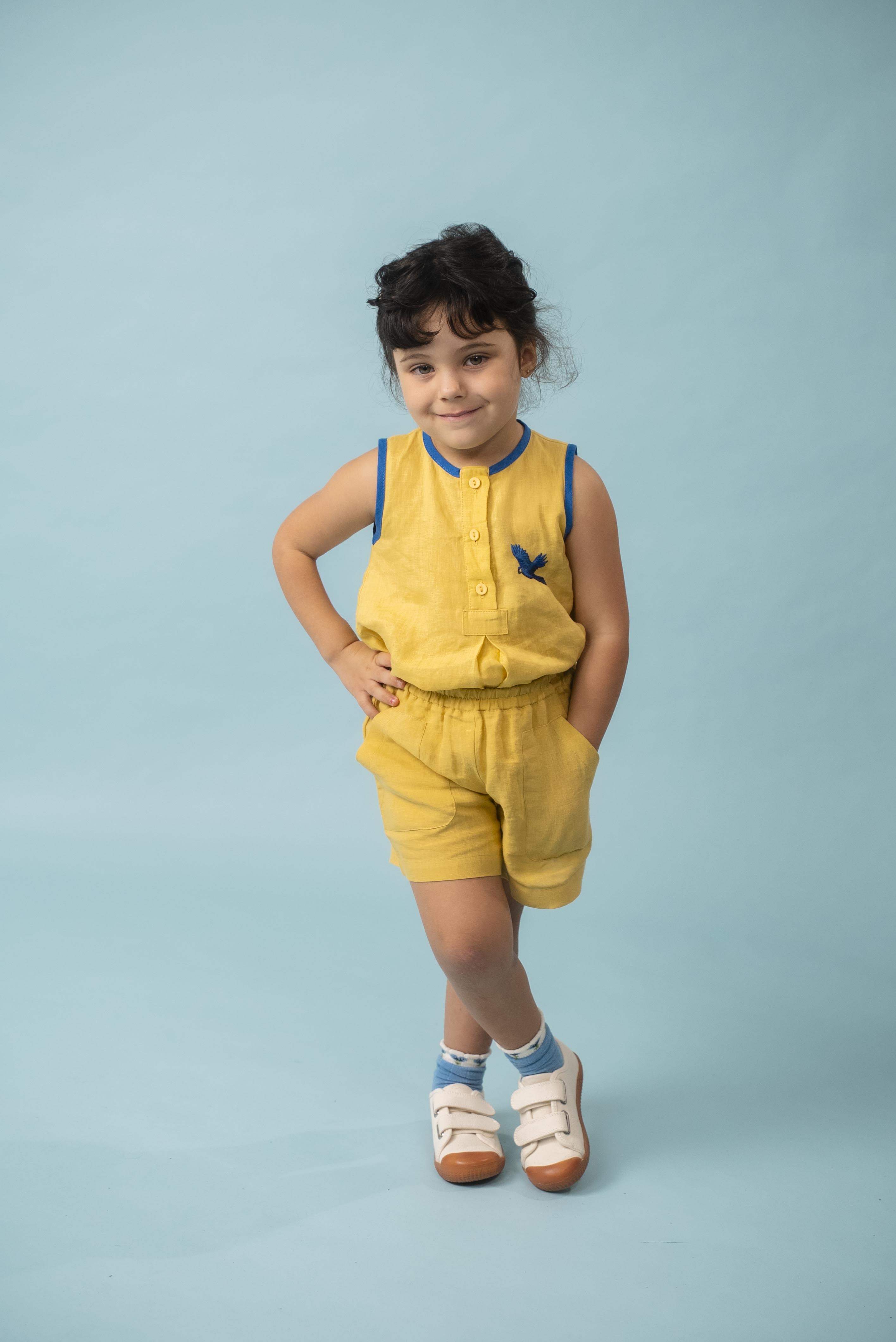 Menina usando shorts infantil amarelo em linho puro com blusa bordada de arara azul