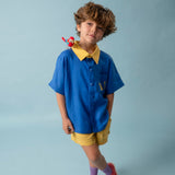 Menino usando shorts infantil amarelo em linho puro combinado com camisa azul e amarela bordada