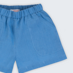 Shorts infantil em linho puro azul capri com bolsos frontais e cintura elástica para meninos e meninas, visto de frente em detalhe.