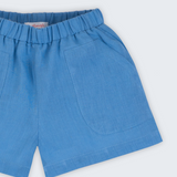 Shorts infantil em linho puro azul capri com bolsos frontais e cintura elástica para meninos e meninas, visto de frente em detalhe.