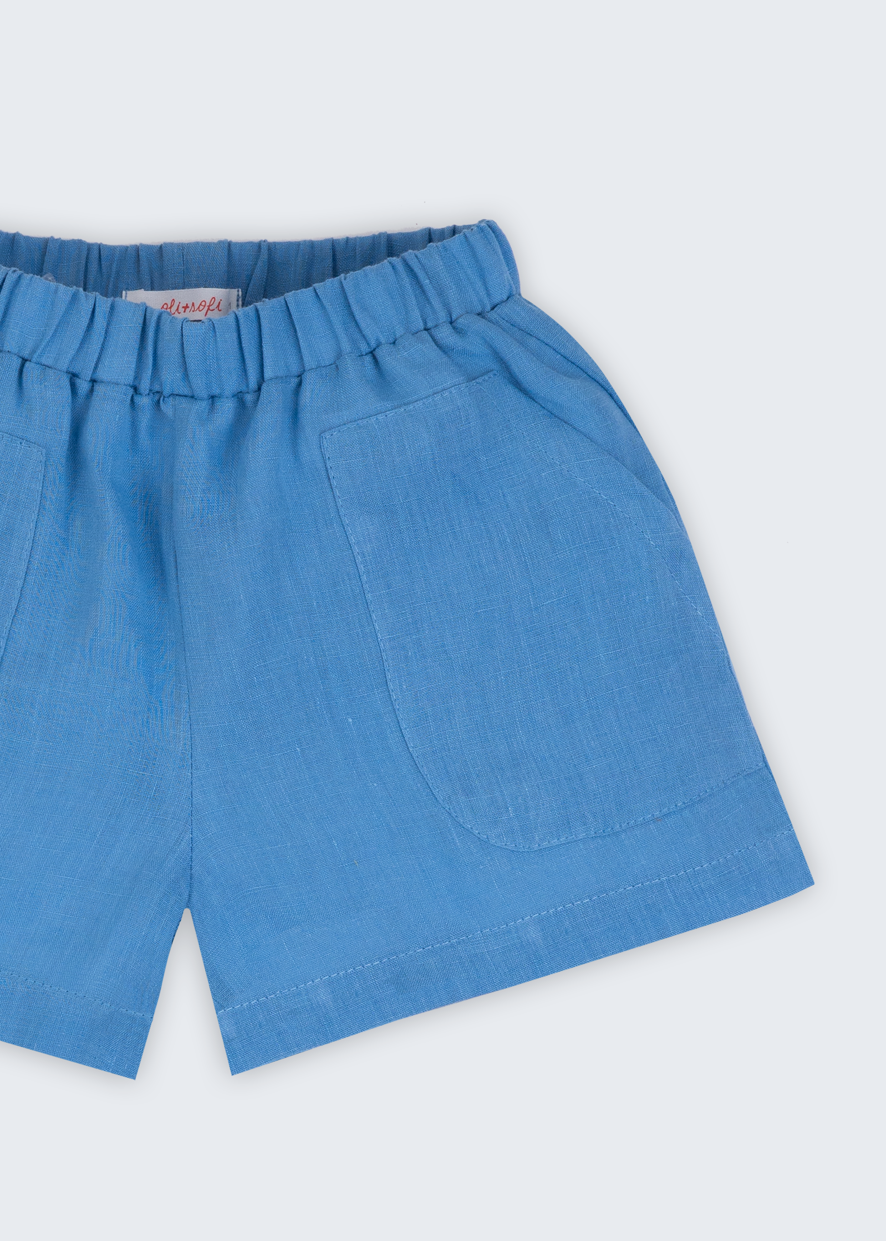 Shorts infantil em linho puro azul capri com bolsos frontais e cintura elástica para meninos e meninas, visto de frente em detalhe.