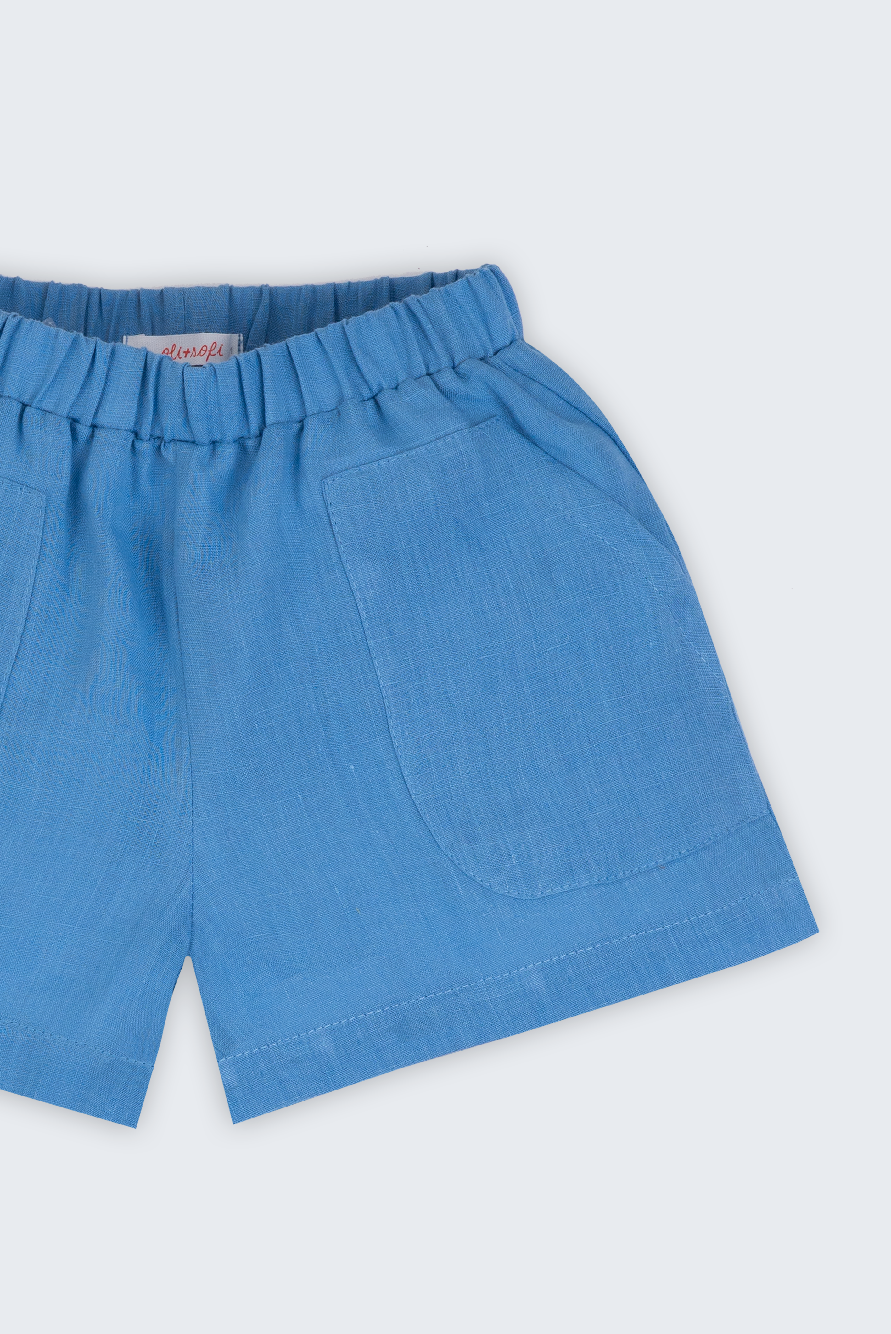 Shorts infantil em linho puro azul capri com bolsos frontais e cintura elástica para meninos e meninas, visto de frente em detalhe.