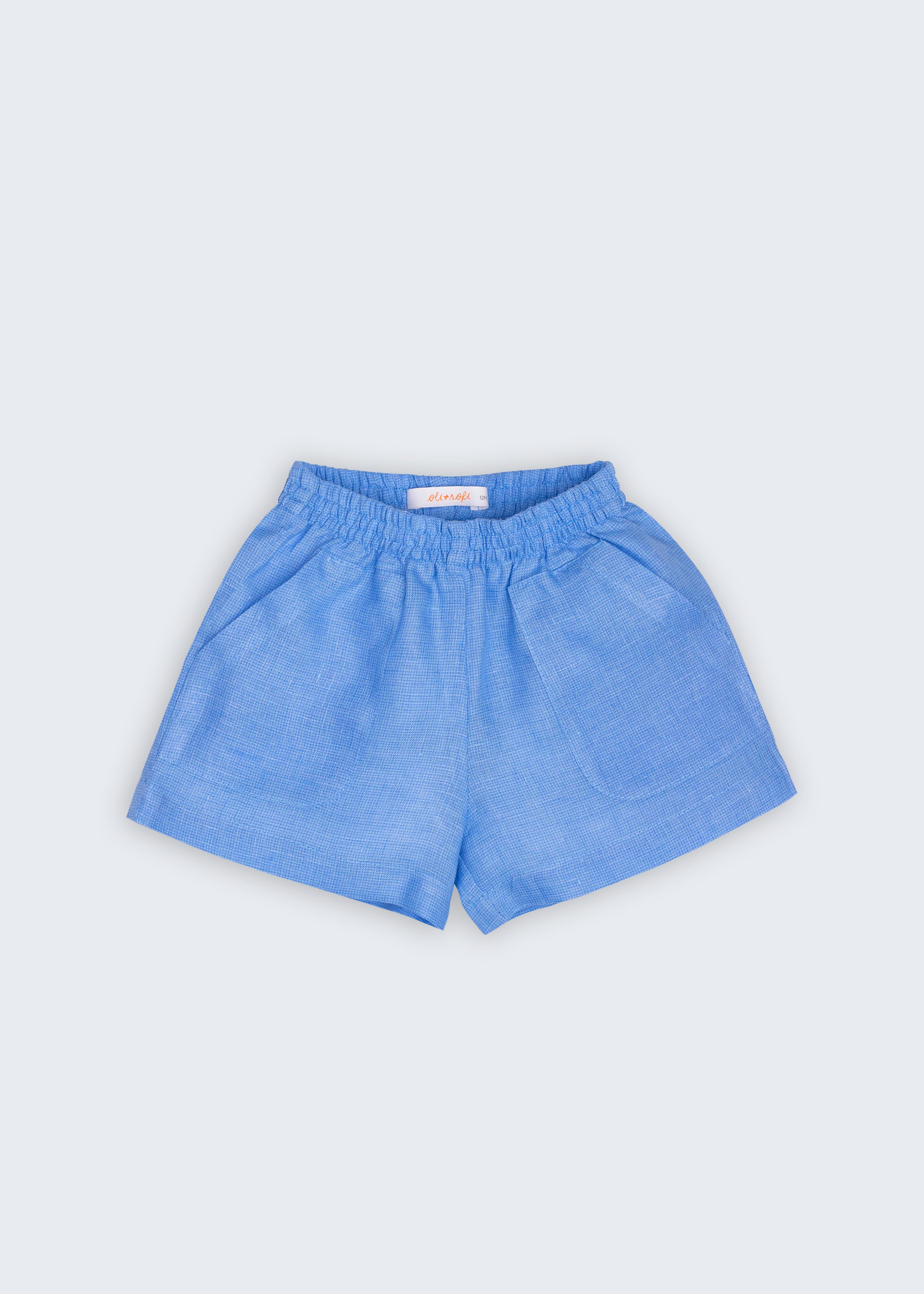 Shorts Chico infantil em 100% linho azul índigo claro, fotografado de frente, com cintura de elástico e bolsos frontais.