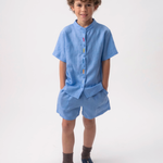 Menino vestindo Shorts Chico infantil em linho azul índigo claro, combinado com camisa azul no mesmo tom.