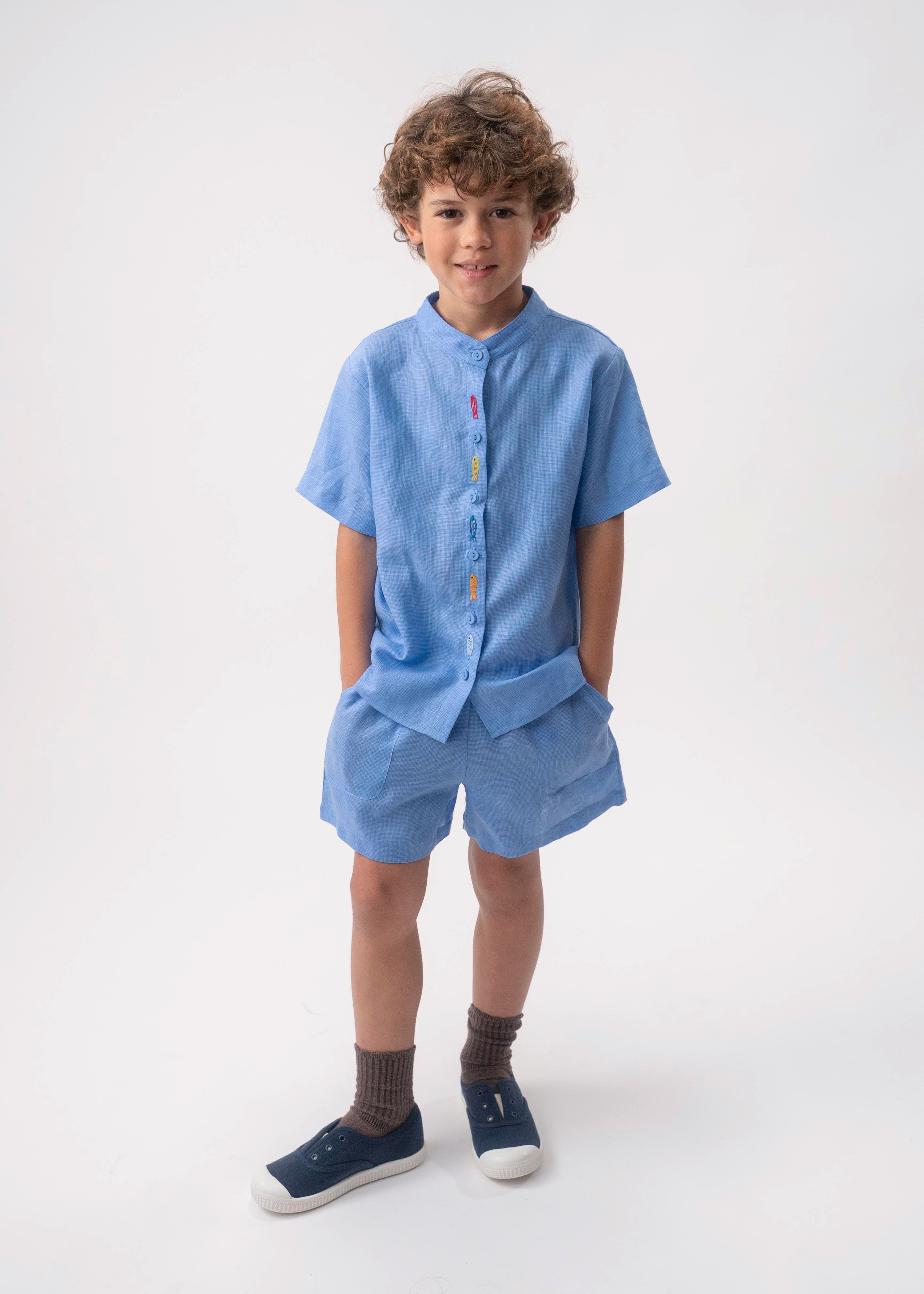 Menino vestindo Shorts Chico infantil em linho azul índigo claro, combinado com camisa azul no mesmo tom.